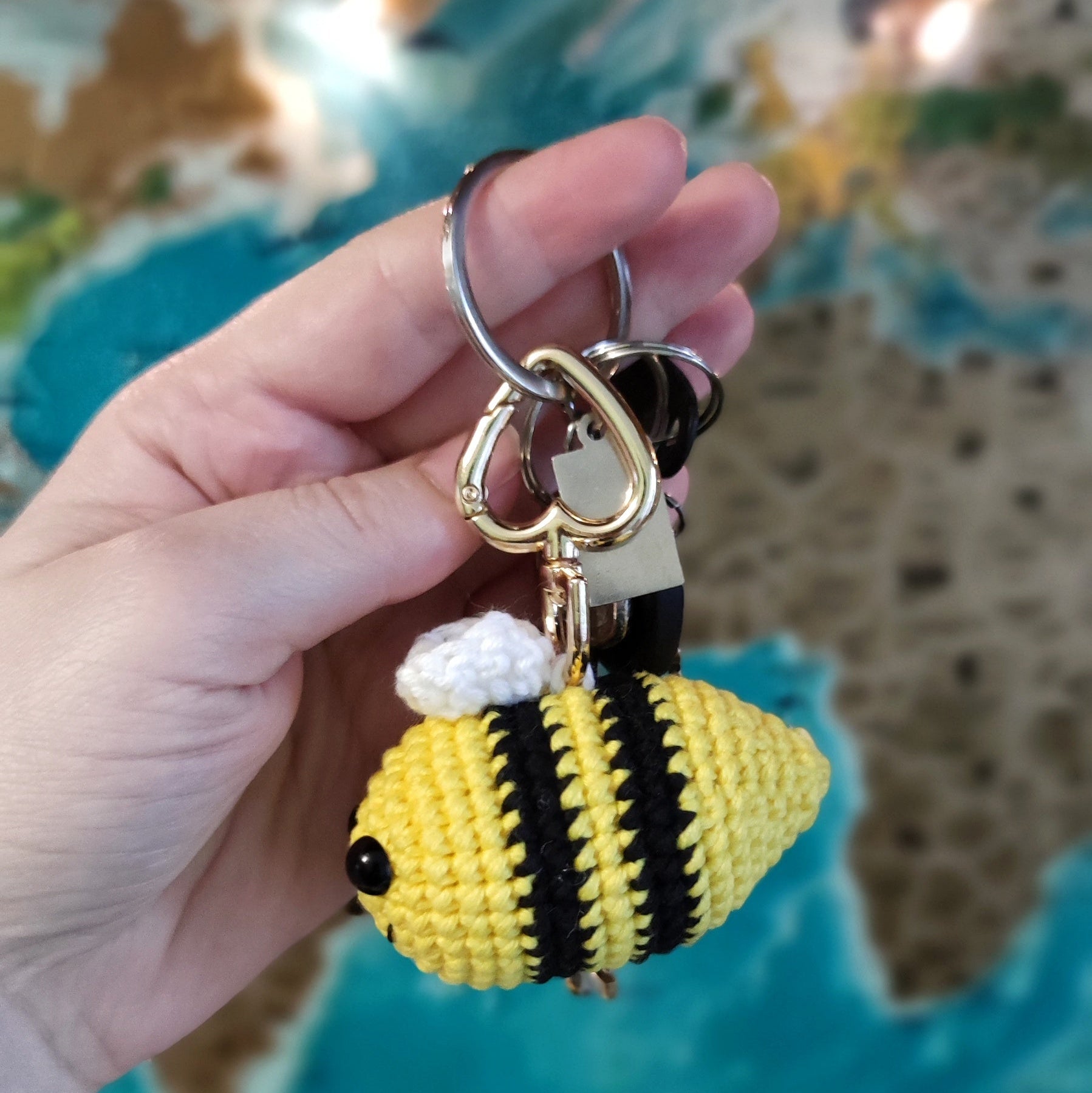 Hand holding a handmade crochet bee keychain amigurumi in front of a world map background.
