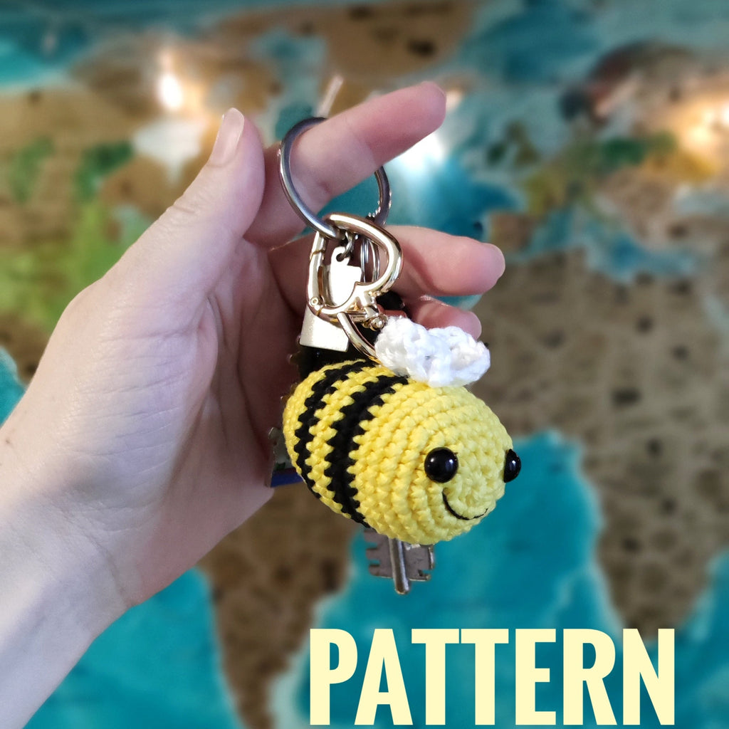 Hand holding a handmade crochet bee keychain amigurumi in front of a world map background.