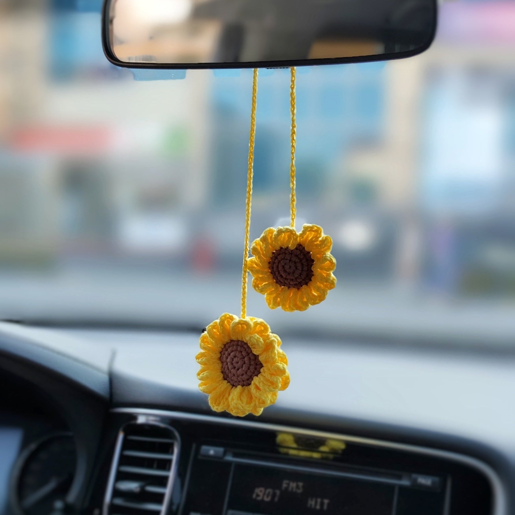 Crochet sunflower car accessory hanging on a cord, bright yellow flower with brown center used as car interior decor.