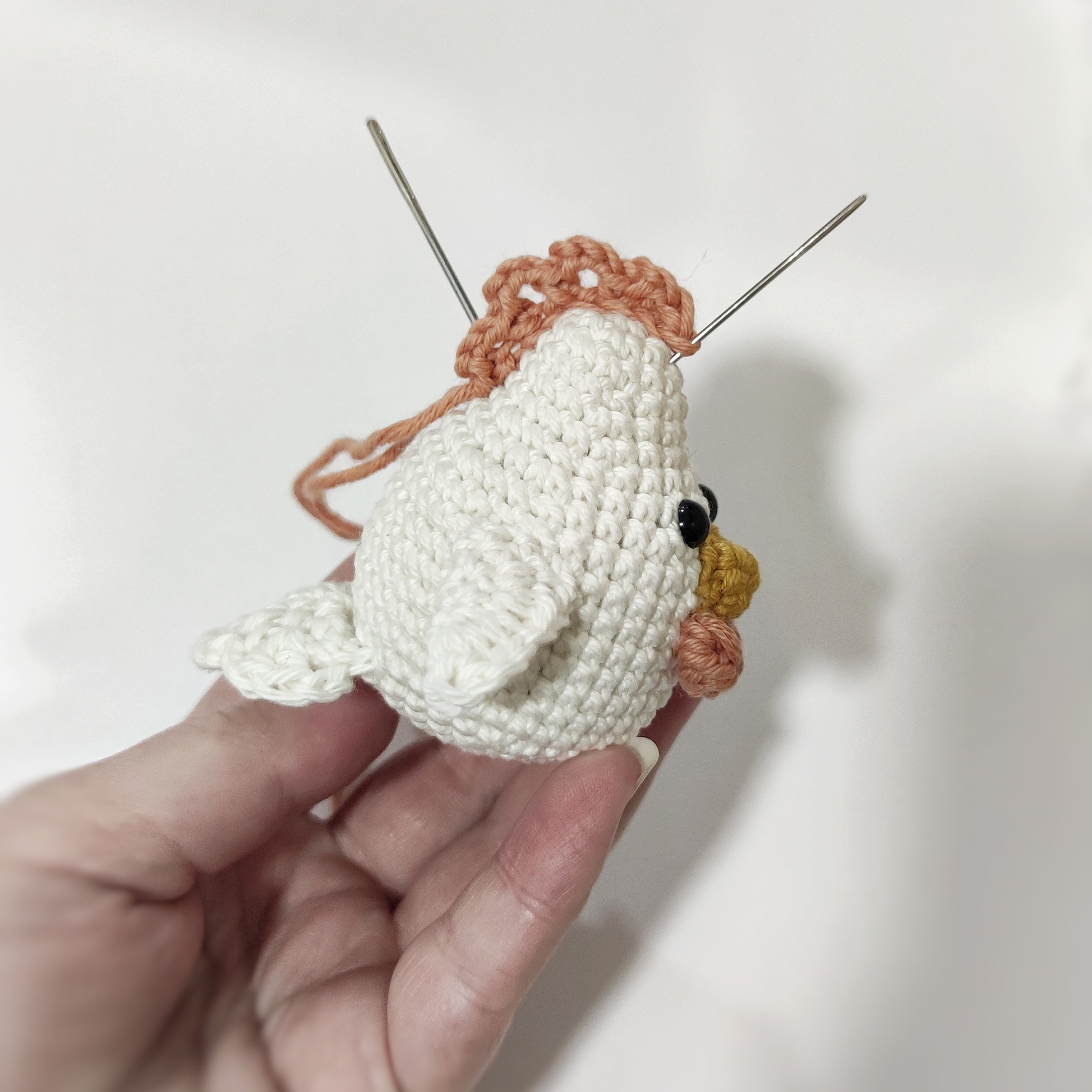 Handmade crochet chicken and rooster amigurumi sitting on a white stand with green plants in the background.