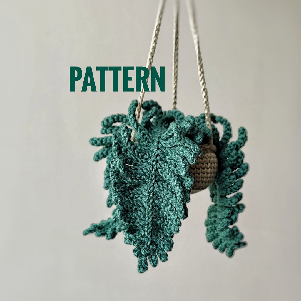 Crochet fern hanging plant pattern with textured green fern leaves and hanging cords on a neutral background.