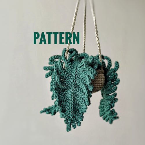 Crochet fern hanging plant pattern with textured green fern leaves and hanging cords on a neutral background.