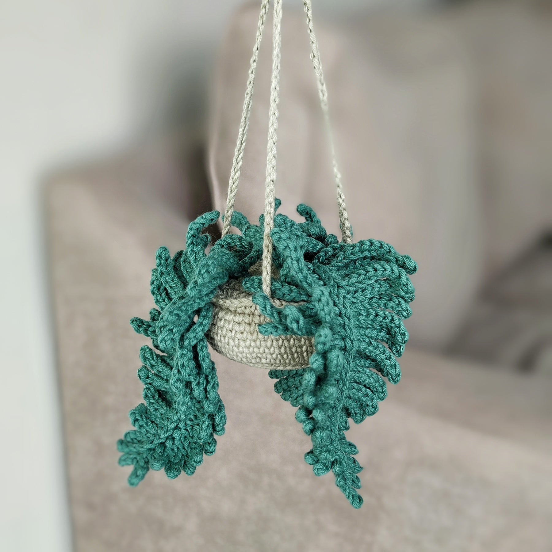 Crochet fern hanging plant pattern with textured green fern leaves and hanging cords on a neutral background.