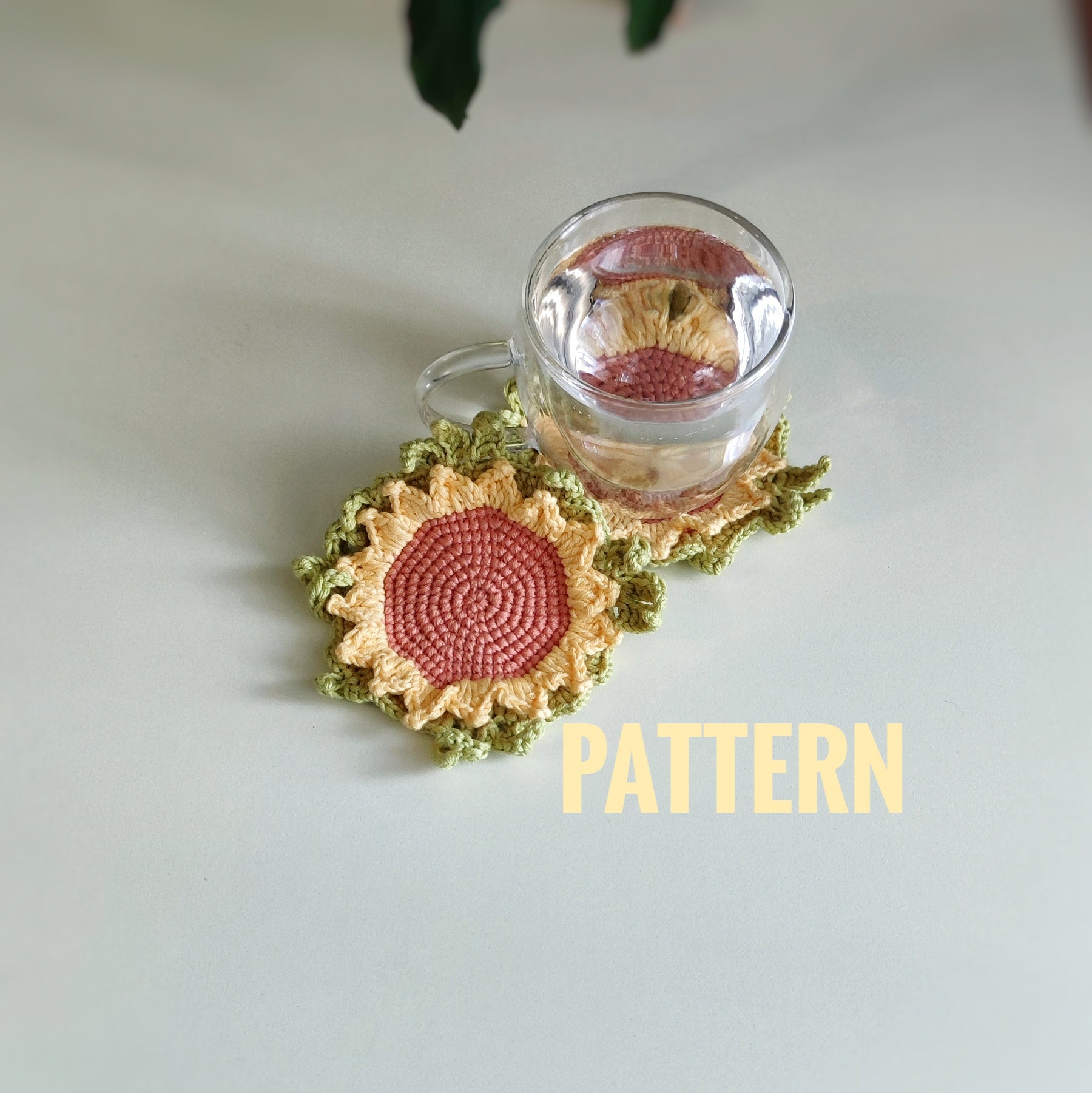 Sunflower crochet coaster with textured petals placed under a clear glass cup on a light surface.