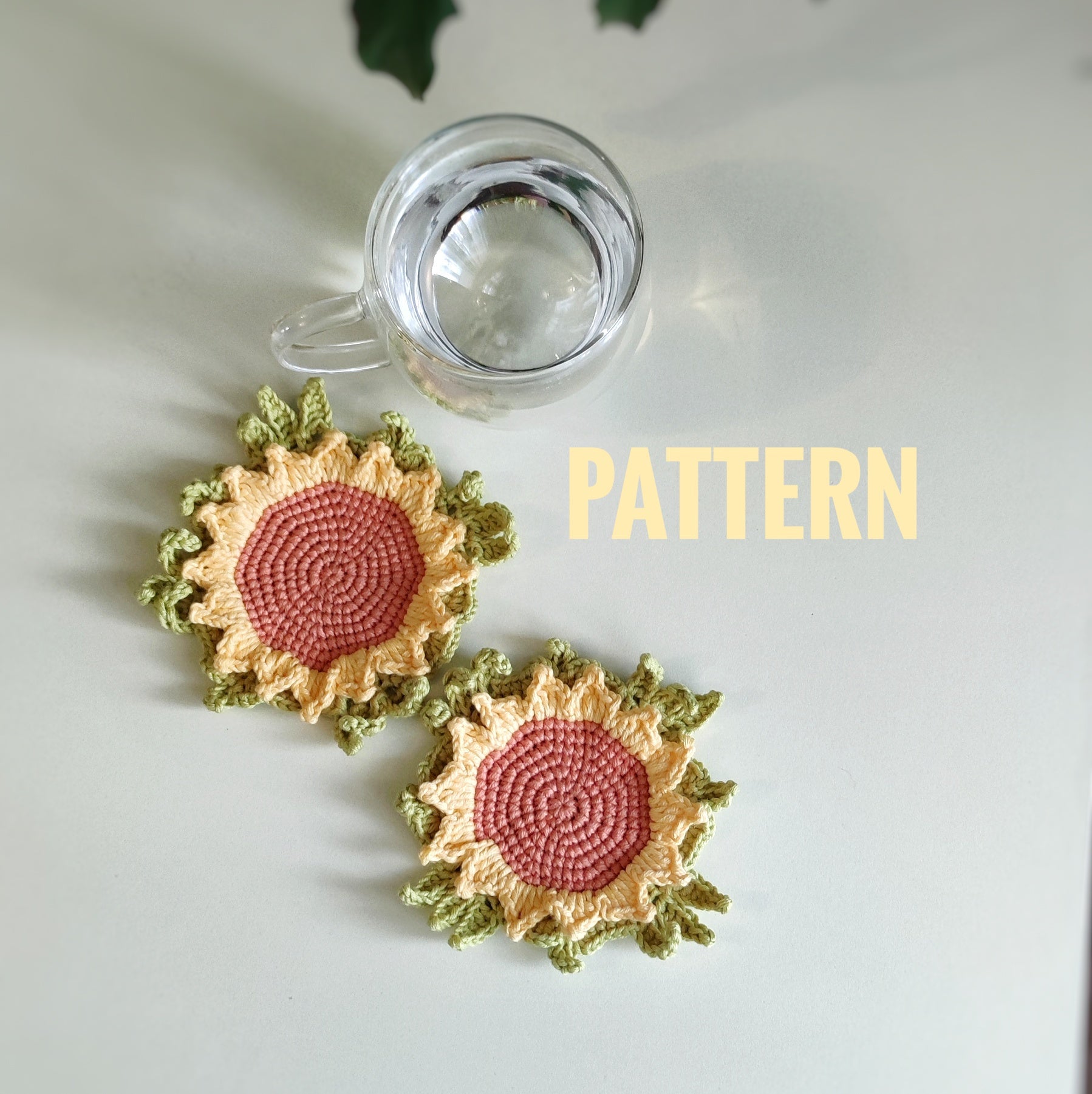 Sunflower crochet coaster with textured petals placed under a clear glass cup on a light surface.