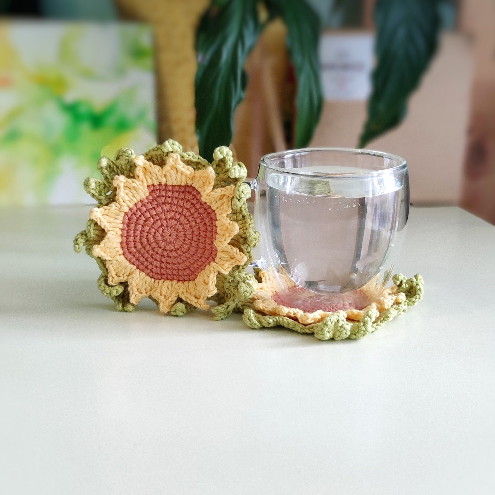Sunflower crochet coaster with textured petals placed under a clear glass cup on a light surface.
