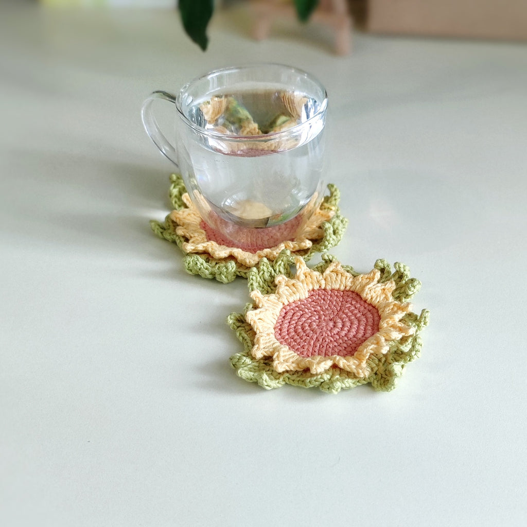 Sunflower crochet coaster with textured petals placed under a clear glass cup on a light surface.