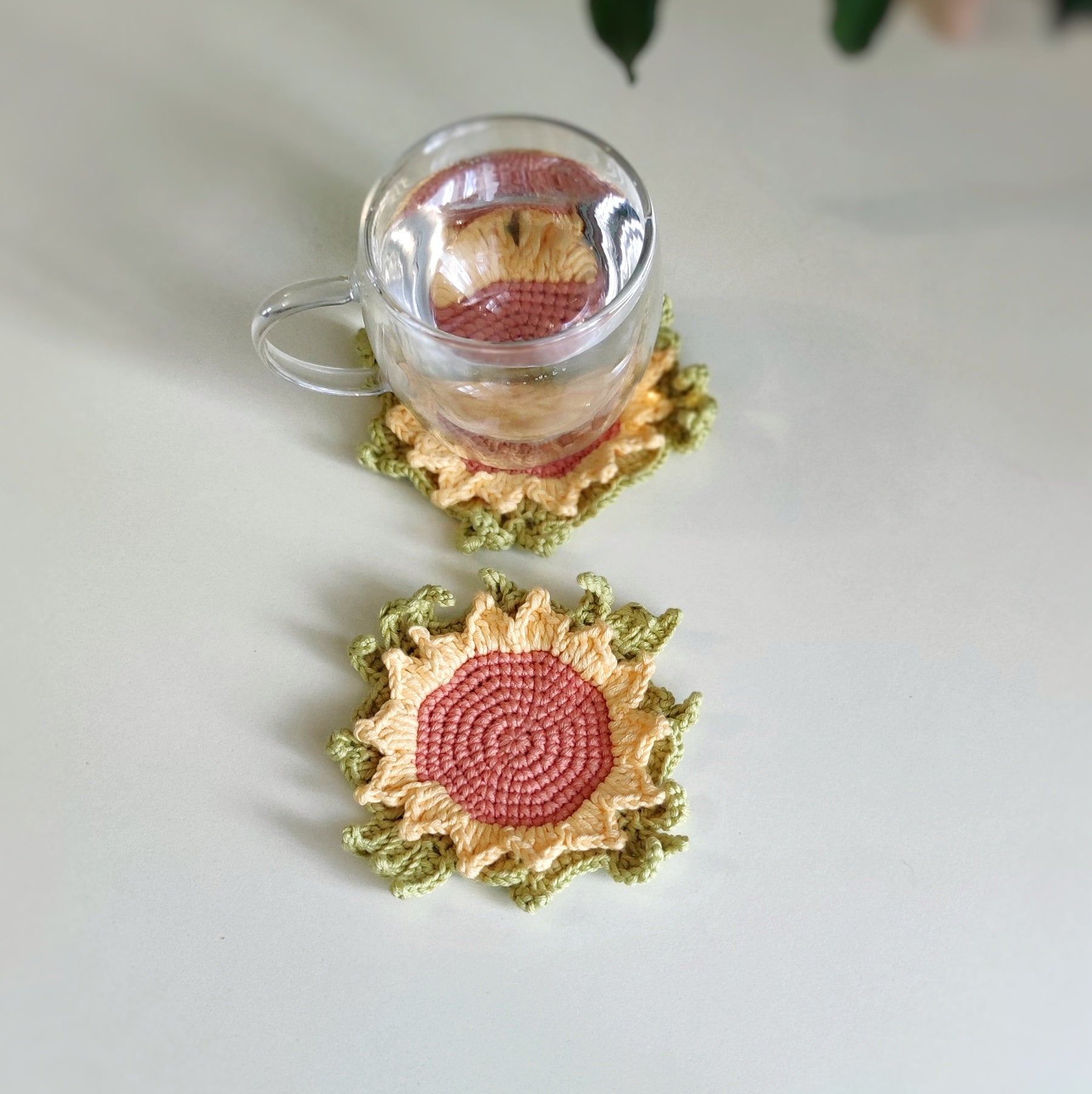 Sunflower crochet coaster with textured petals placed under a clear glass cup on a light surface.