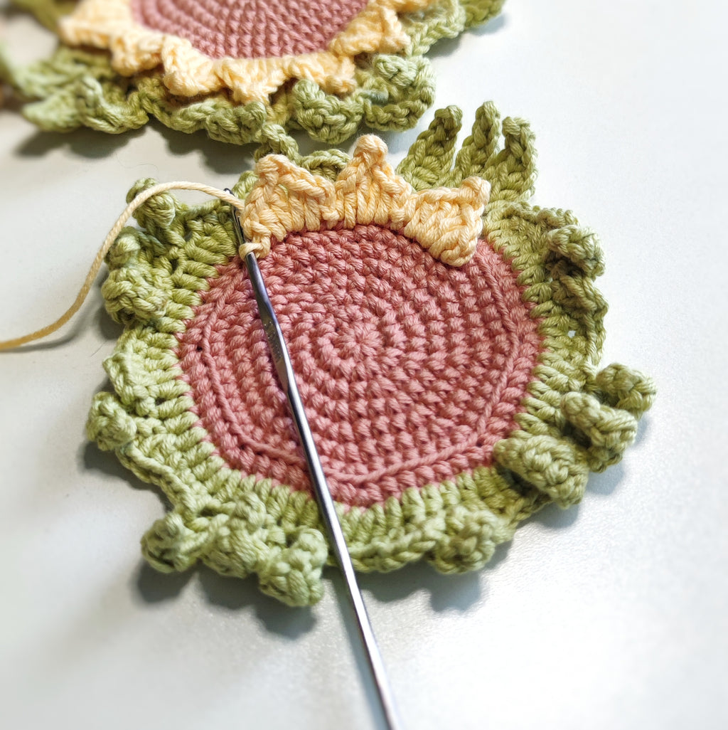 Sunflower crochet coaster with textured petals placed under a clear glass cup on a light surface.