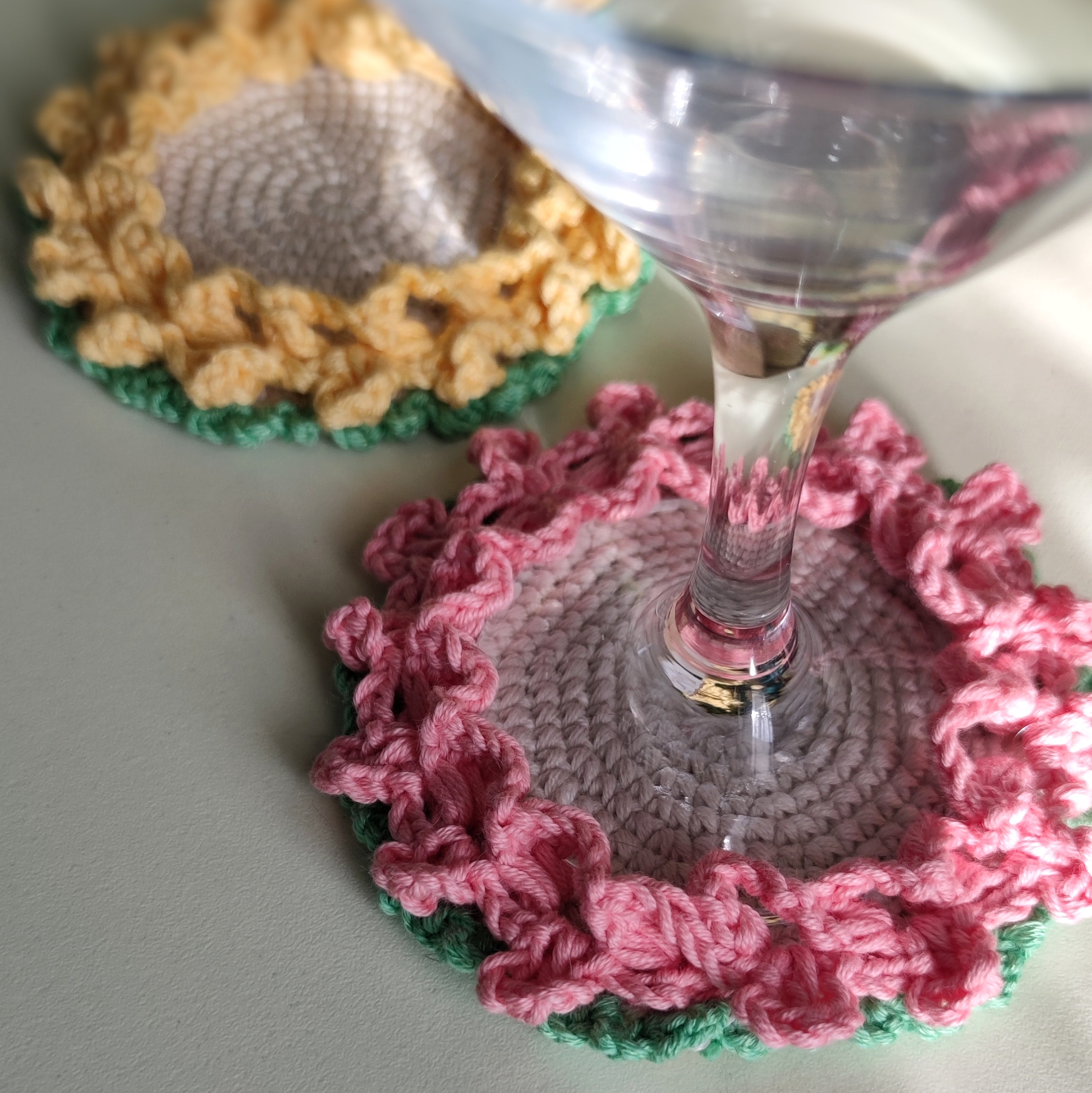 Crochet flower coasters with ruffled edges under cocktail glasses