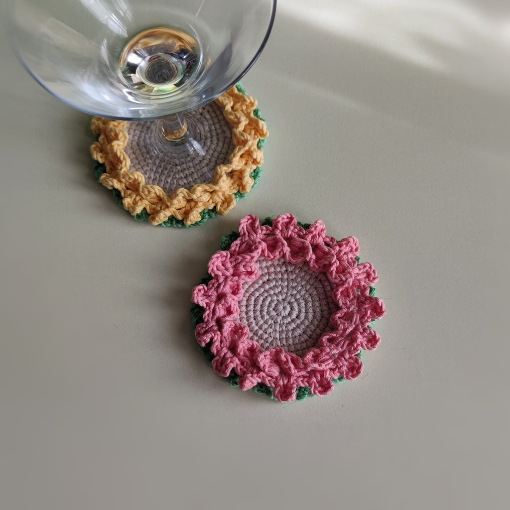 Crochet flower coasters with ruffled edges under cocktail glasses