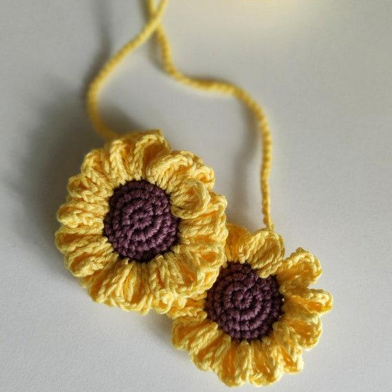 Crochet sunflower car accessory hanging on a cord, bright yellow flower with brown center used as car interior decor.