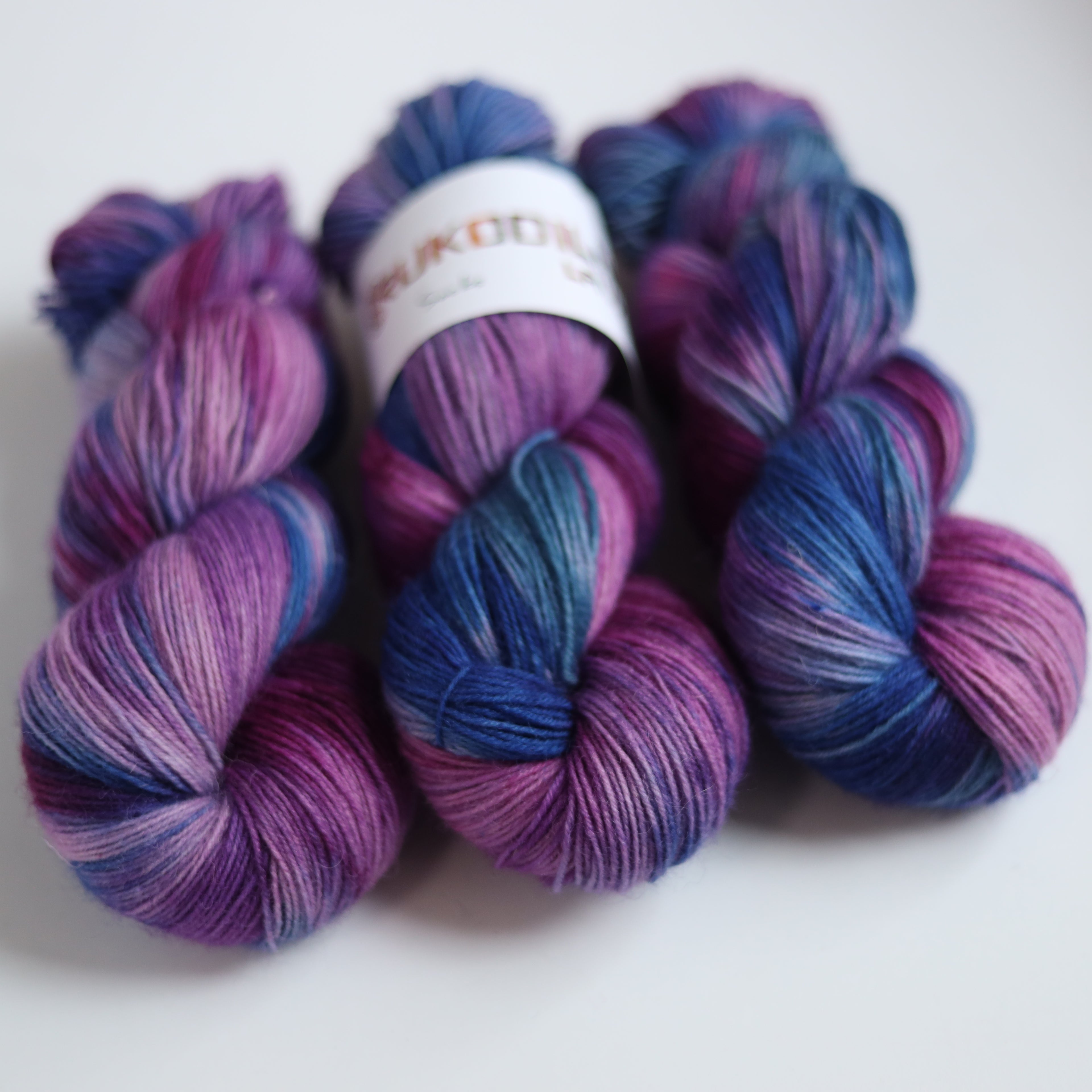 Hand dyed sock yarn in purple, violet, and deep blue tones with a knitted sock sample on wooden sock blocker, fingering weight 4-ply yarn