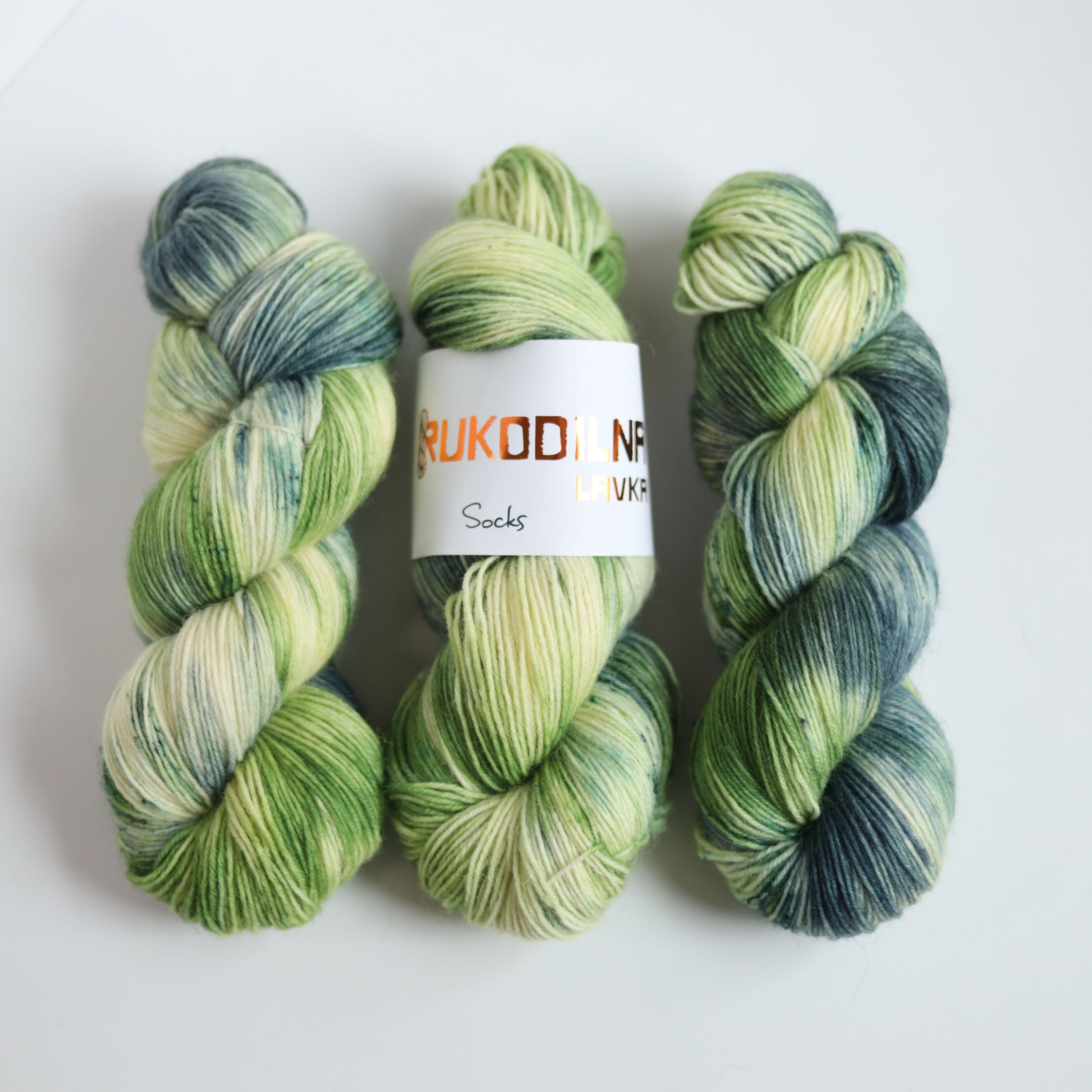 Hand dyed sock yarn in green and blue tones made from wool and polyamide, three skeins on a white background