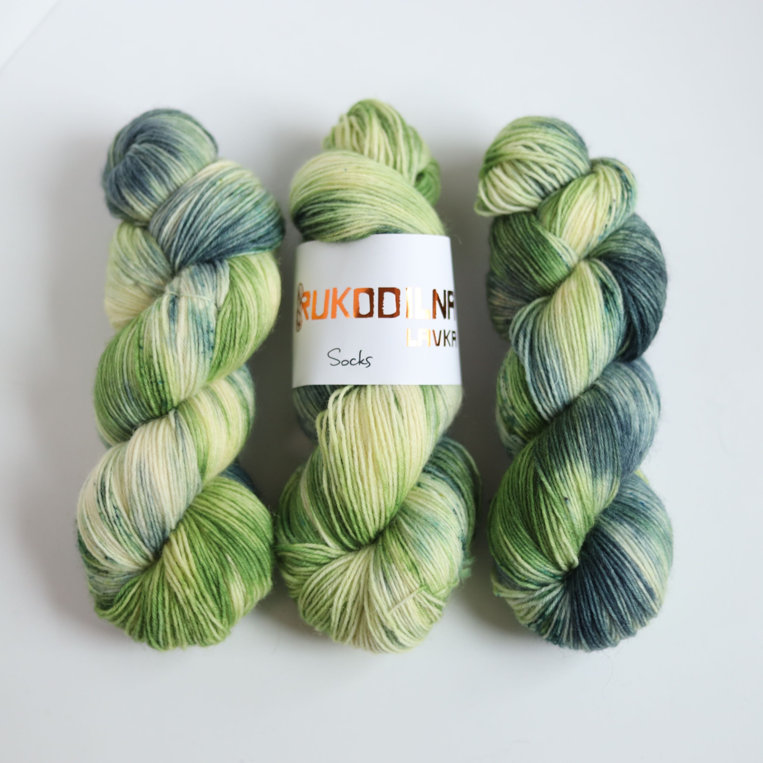 Hand dyed sock yarn in green and blue tones made from wool and polyamide, three skeins on a white background