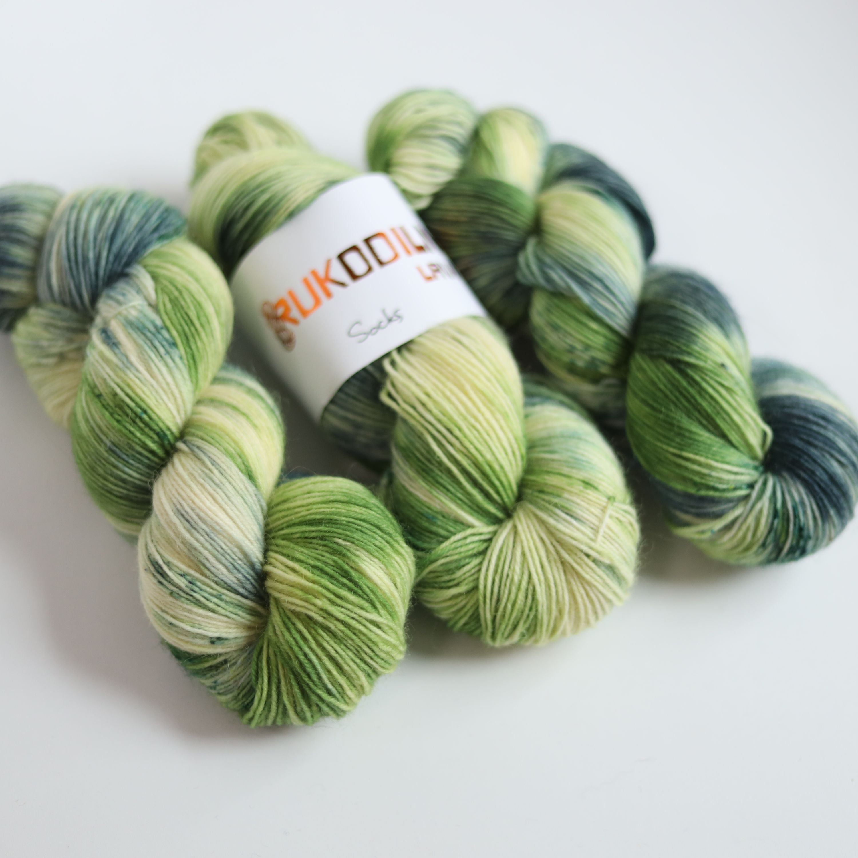 Hand dyed sock yarn in green and blue tones made from wool and polyamide, three skeins on a white background