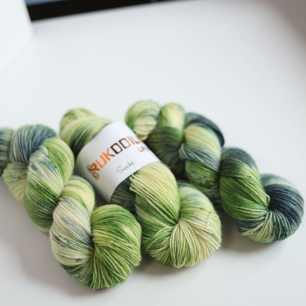 Hand dyed sock yarn in green and blue tones made from wool and polyamide, three skeins on a white background