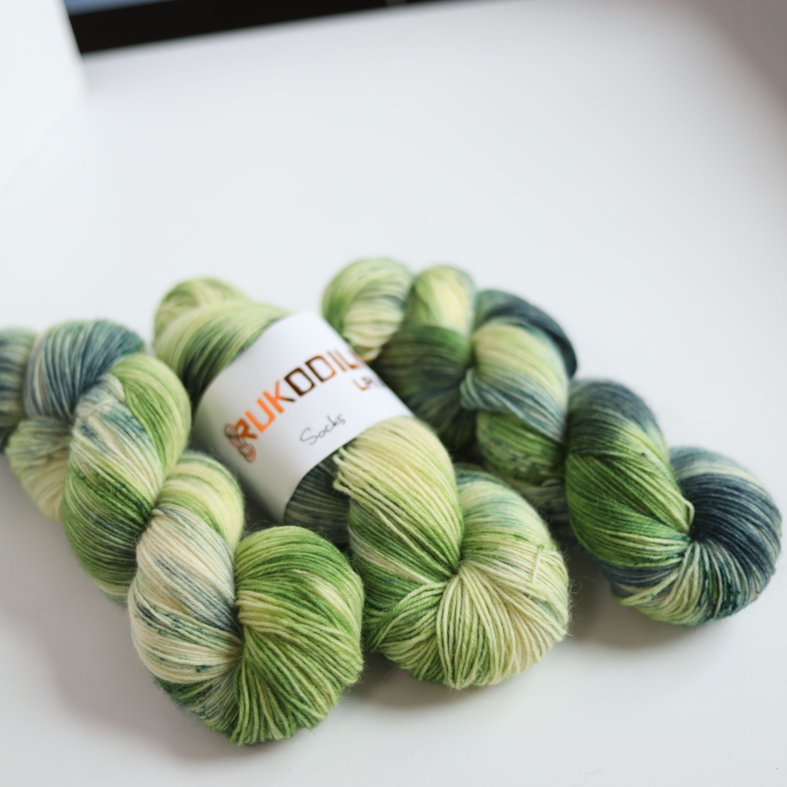 Hand dyed sock yarn in green and blue tones made from wool and polyamide, three skeins on a white background