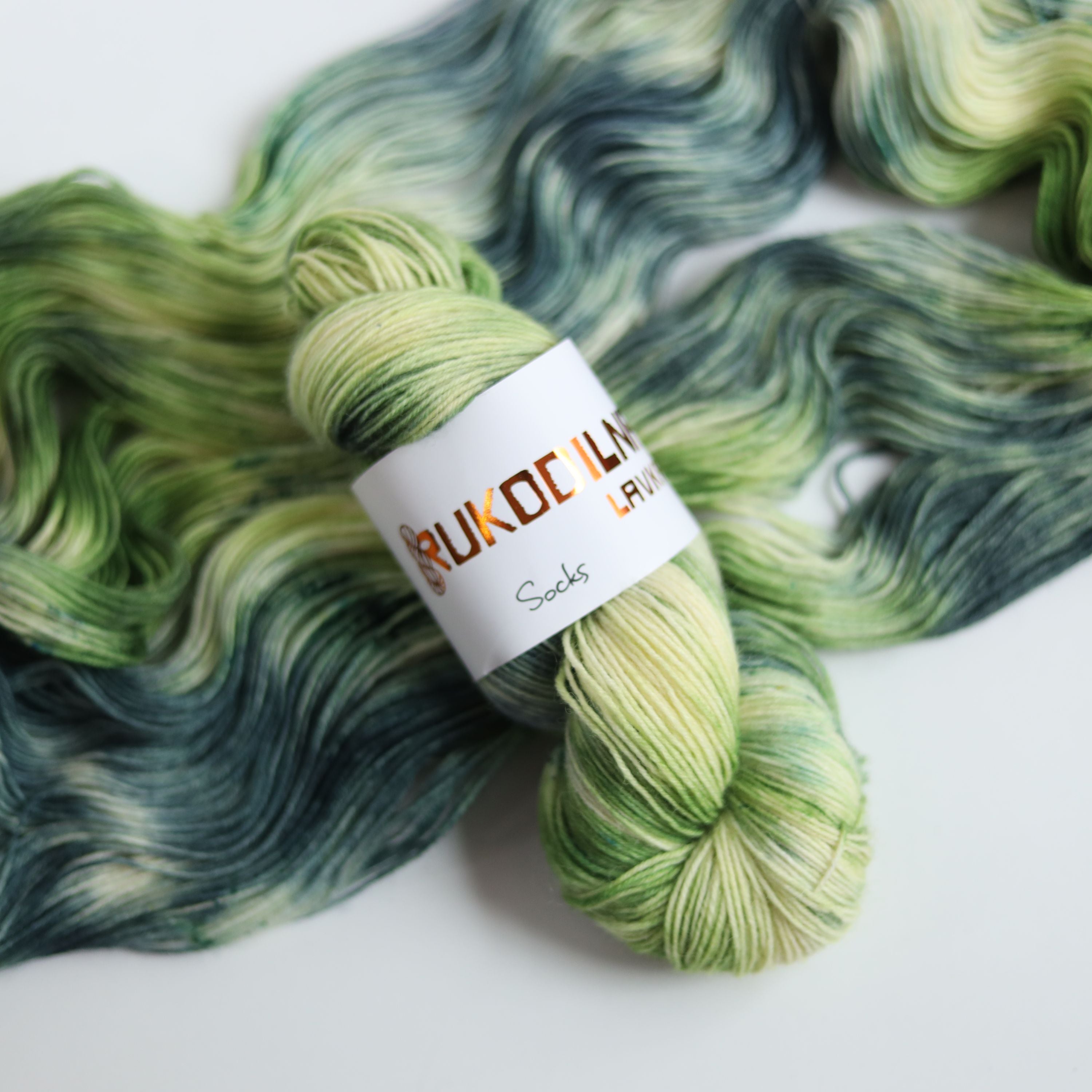 Hand dyed sock yarn in green and blue tones made from wool and polyamide, three skeins on a white background