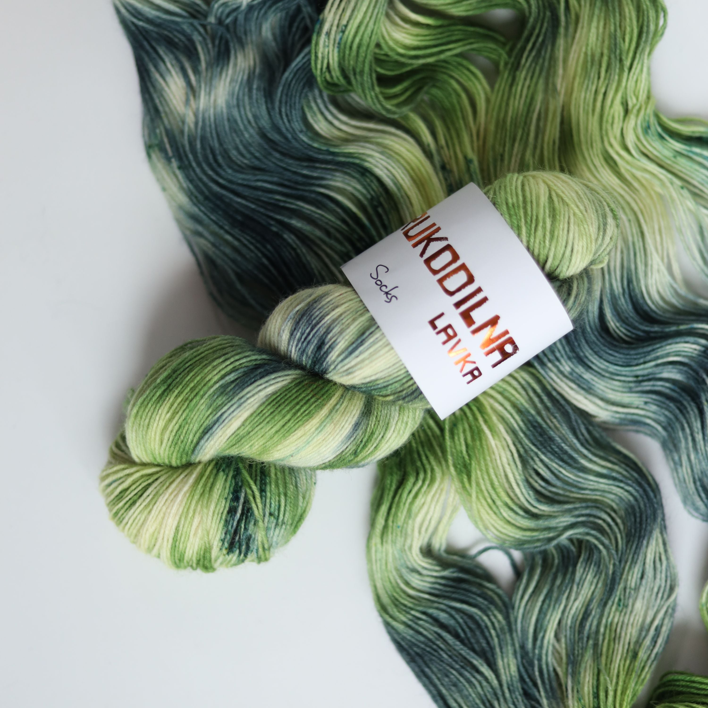 Hand dyed sock yarn in green and blue tones made from wool and polyamide, three skeins on a white background