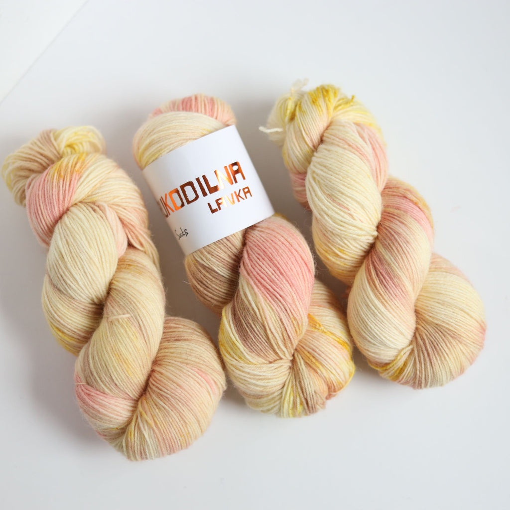Hand dyed sock yarn in peach and yellow tones made from wool and polyamide, one skein on a light background