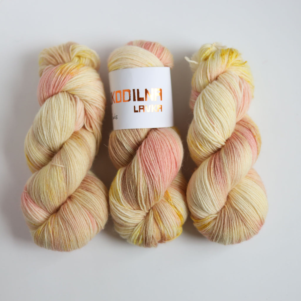 Hand dyed sock yarn in peach and yellow tones made from wool and polyamide, one skein on a light background