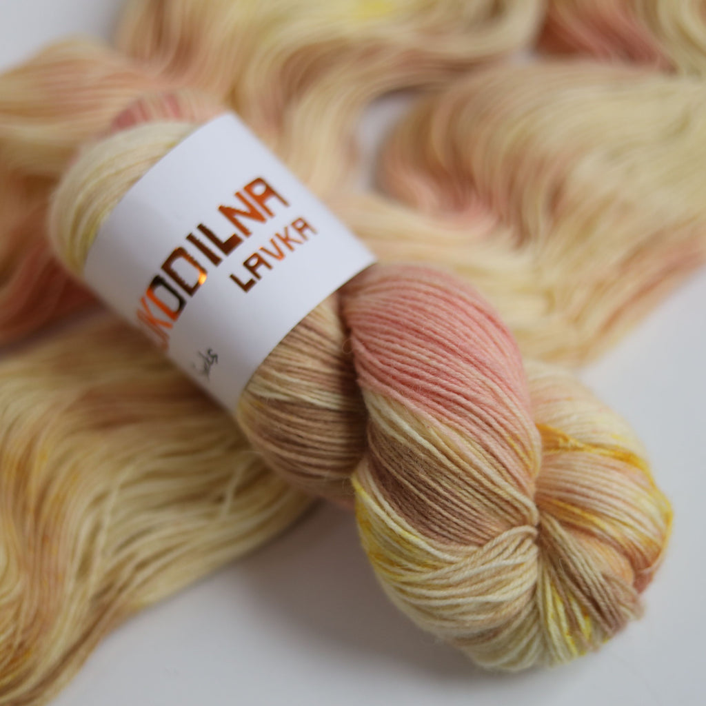 Hand dyed sock yarn in peach and yellow tones made from wool and polyamide, one skein on a light background