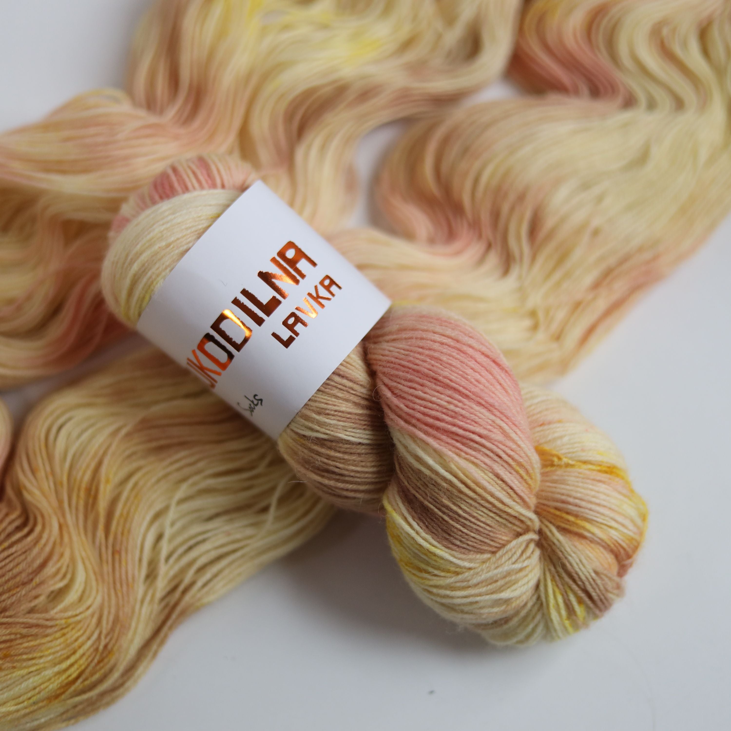 Hand dyed sock yarn in peach and yellow tones made from wool and polyamide, one skein on a light background