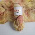Hand dyed sock yarn in peach and yellow tones made from wool and polyamide, one skein on a light background
