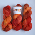 Three skeins of hand dyed superwash merino sock yarn in warm orange and red tonal shades on a white background