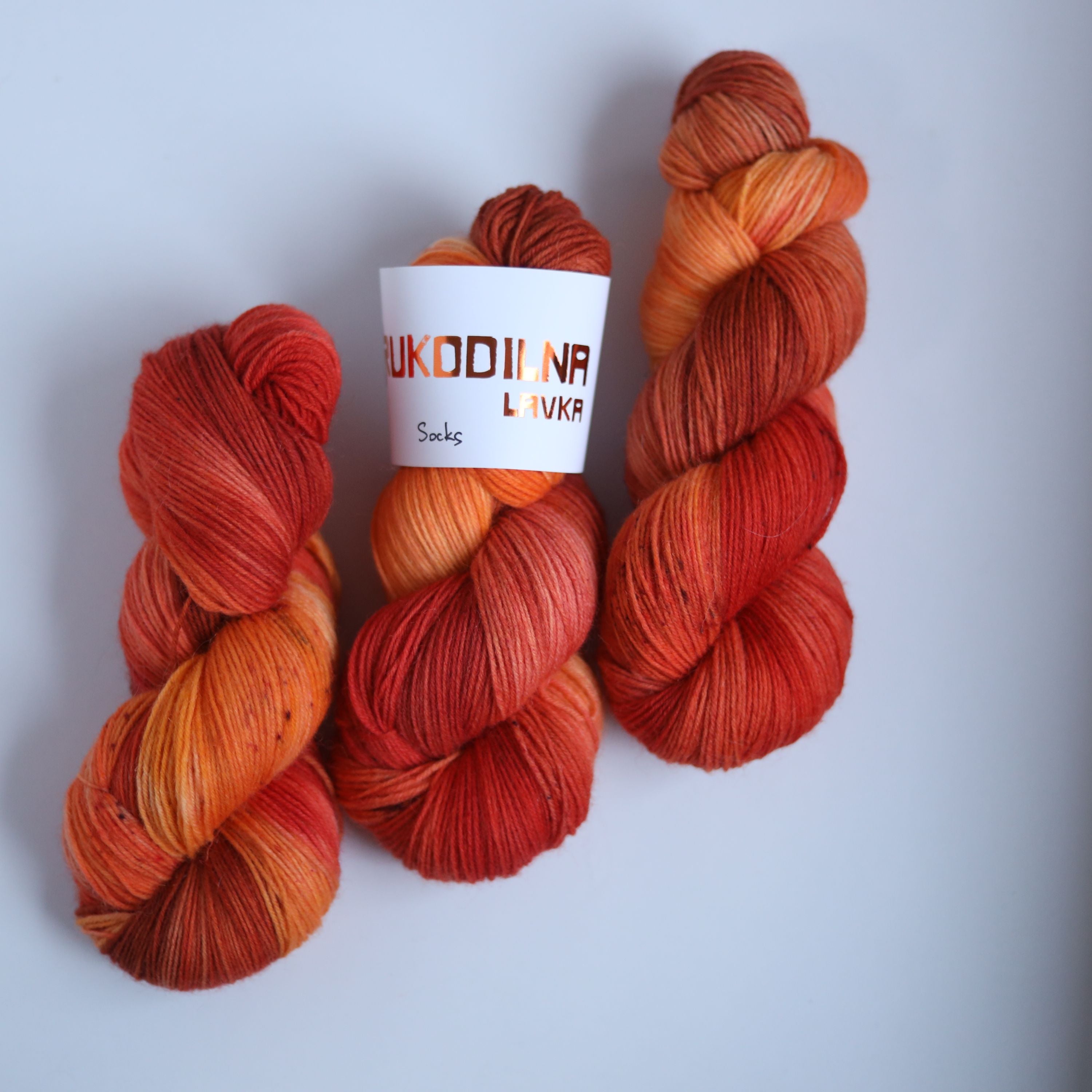 Three skeins of hand dyed superwash merino sock yarn in warm orange and red tonal shades on a white background