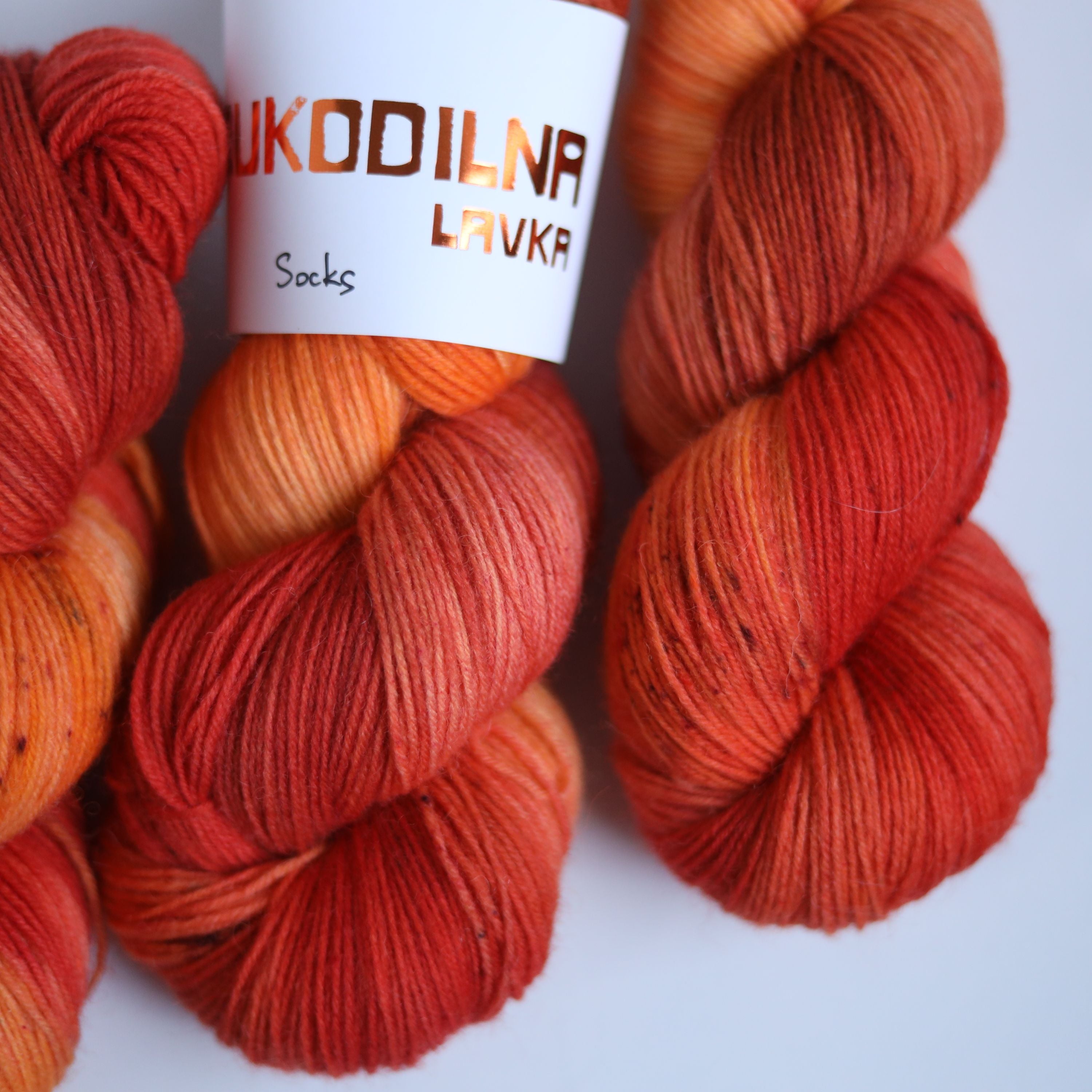Three skeins of hand dyed superwash merino sock yarn in warm orange and red tonal shades on a white background