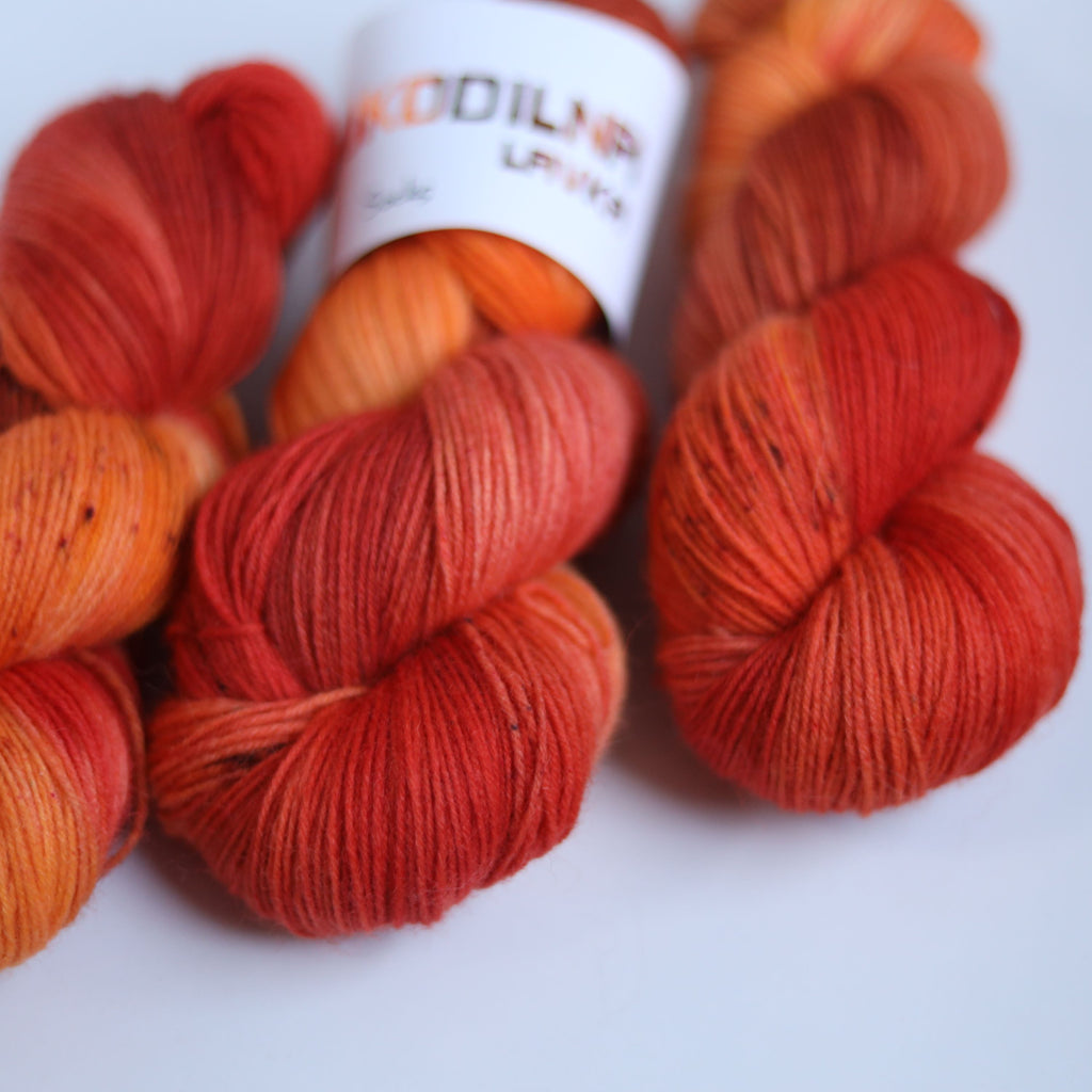 Three skeins of hand dyed superwash merino sock yarn in warm orange and red tonal shades on a white background