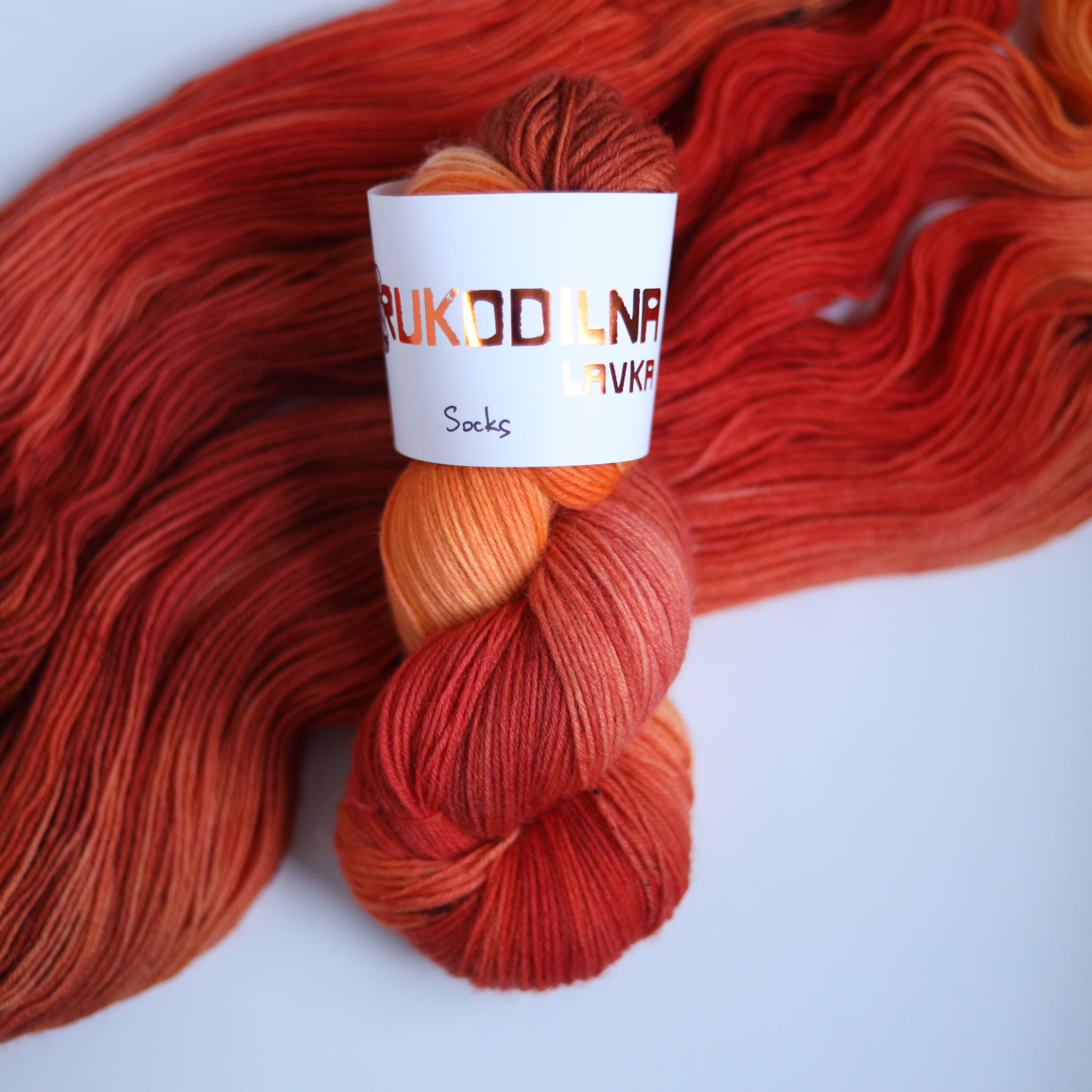Three skeins of hand dyed superwash merino sock yarn in warm orange and red tonal shades on a white background