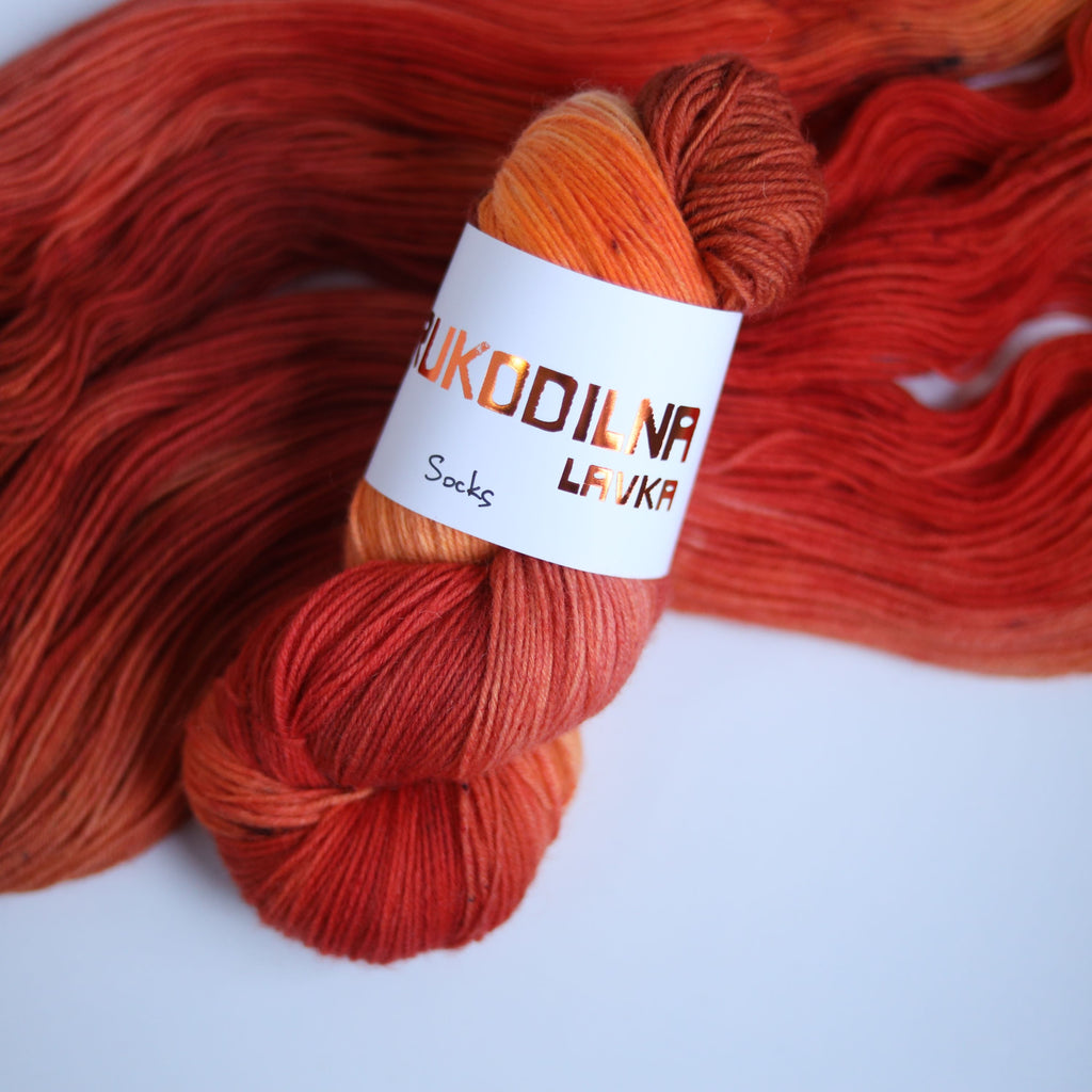 Three skeins of hand dyed superwash merino sock yarn in warm orange and red tonal shades on a white background