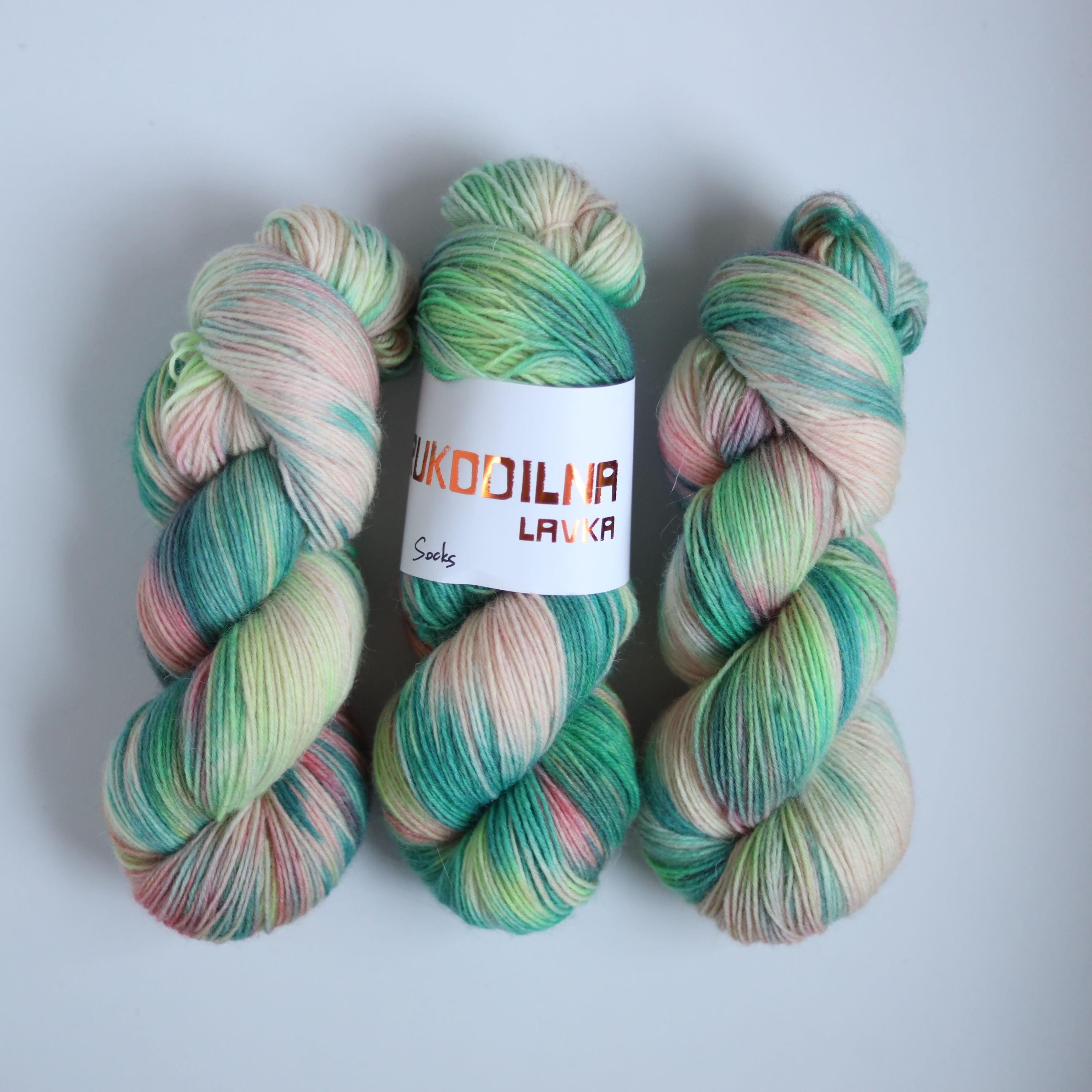 Hand dyed superwash merino sock yarn in neon green variegated shades with soft pink and beige tones on a white background