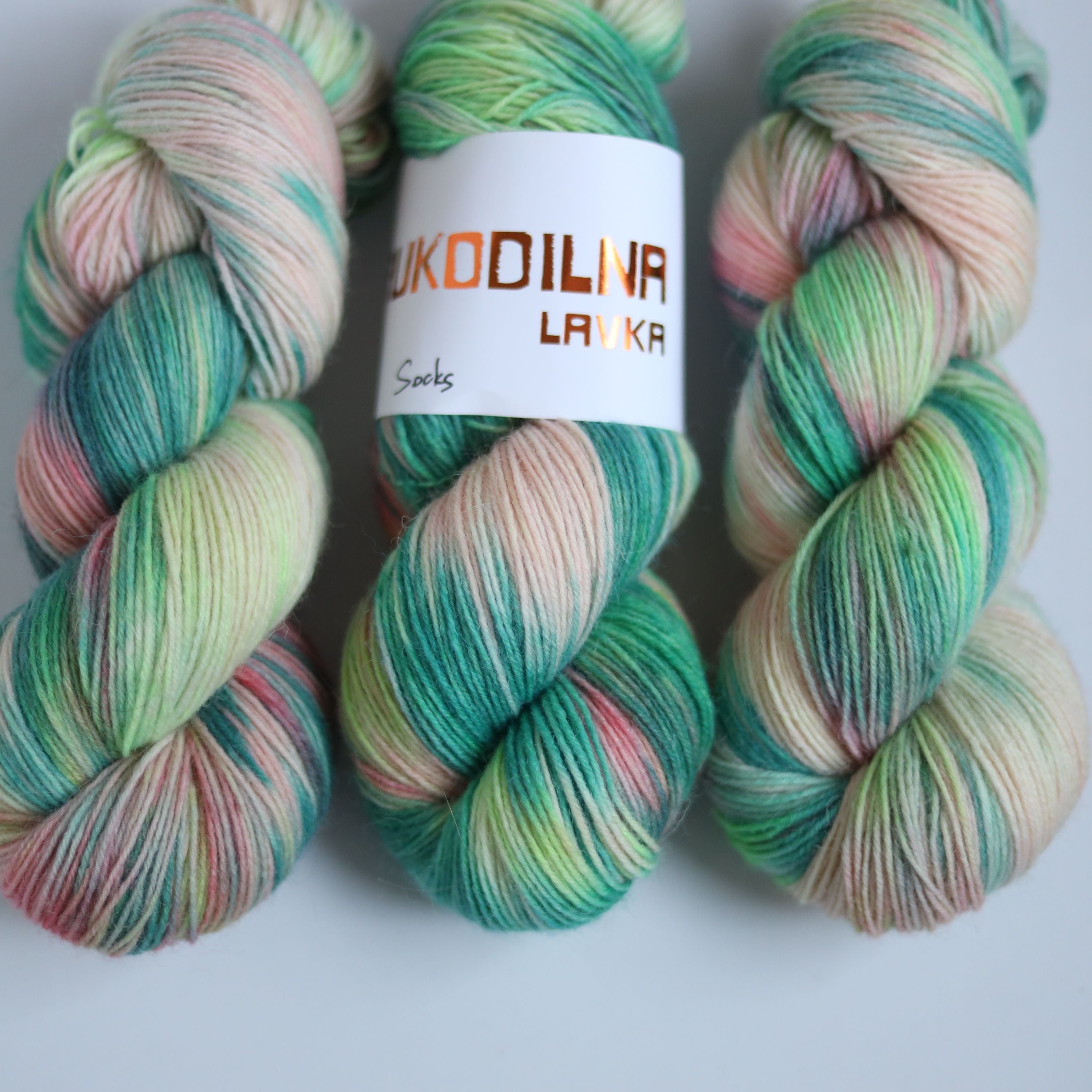 Hand dyed superwash merino sock yarn in neon green variegated shades with soft pink and beige tones on a white background