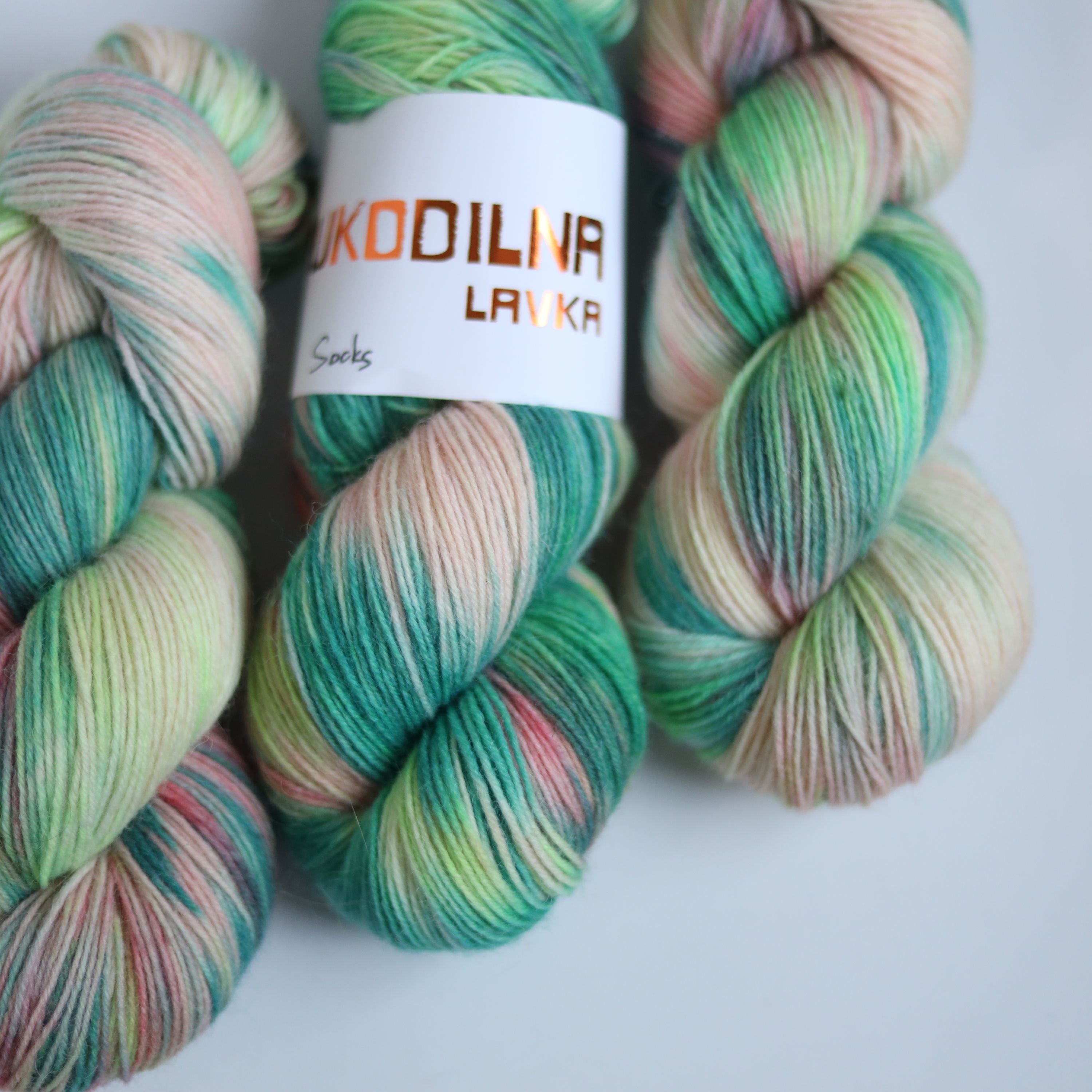 Hand dyed superwash merino sock yarn in neon green variegated shades with soft pink and beige tones on a white background