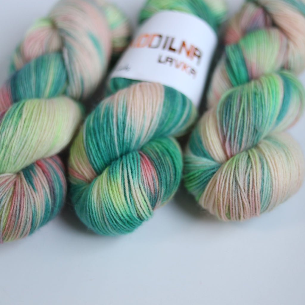 Hand dyed superwash merino sock yarn in neon green variegated shades with soft pink and beige tones on a white background