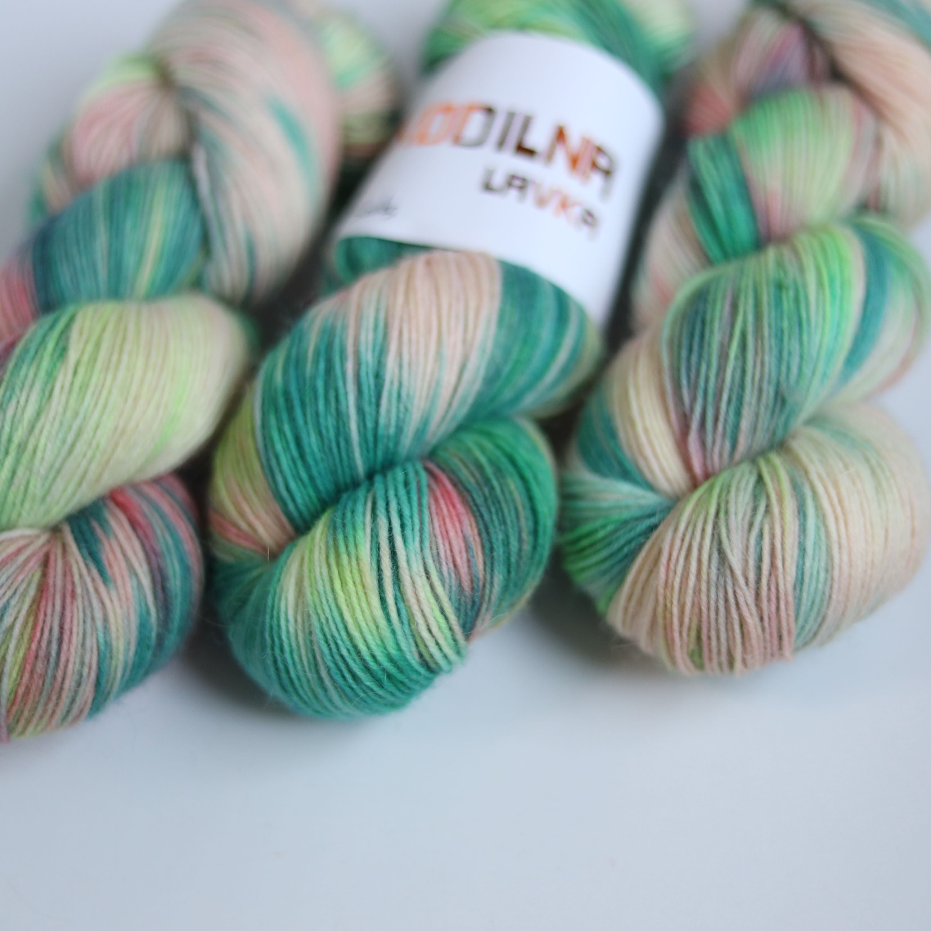 Hand dyed superwash merino sock yarn in neon green variegated shades with soft pink and beige tones on a white background