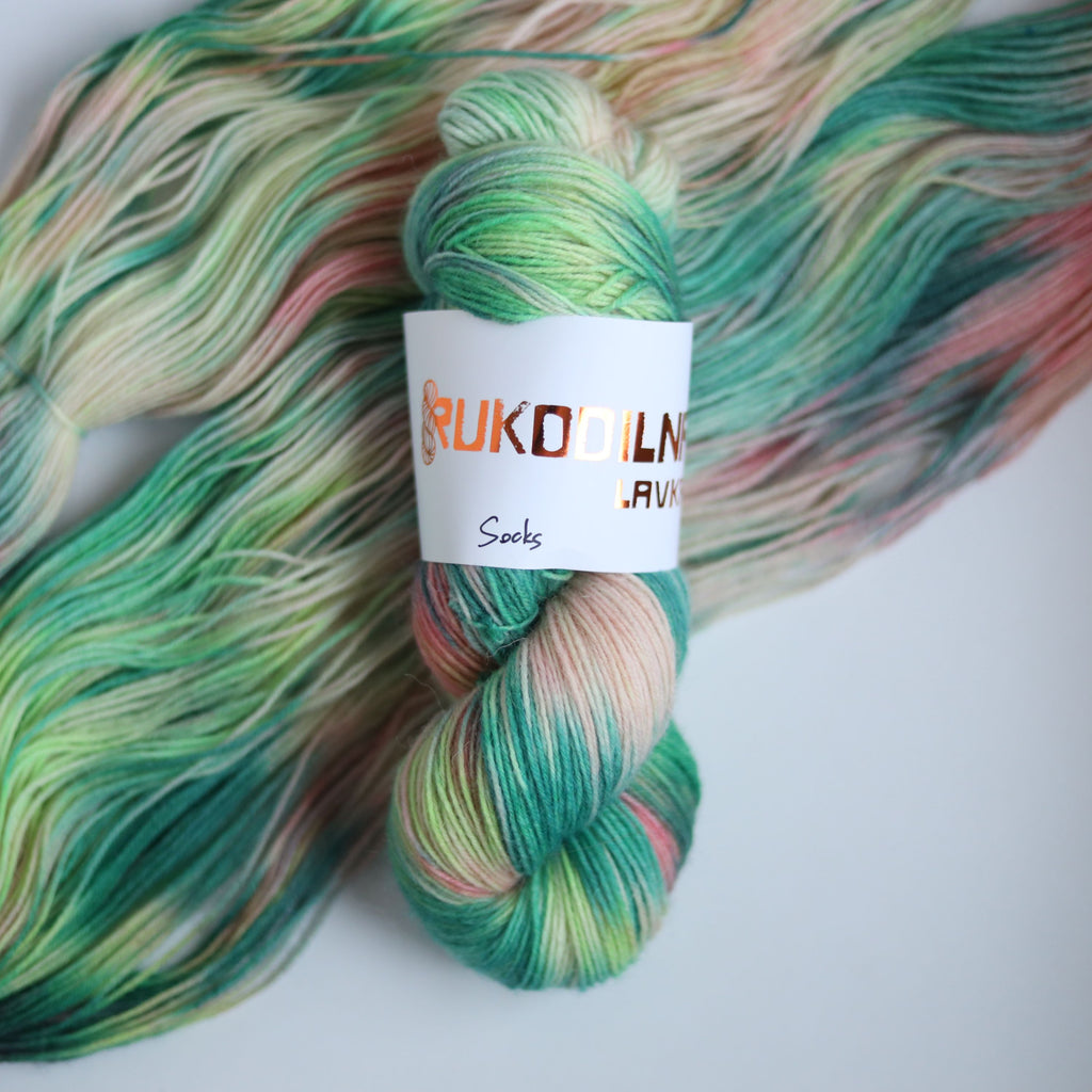 Hand dyed superwash merino sock yarn in neon green variegated shades with soft pink and beige tones on a white background