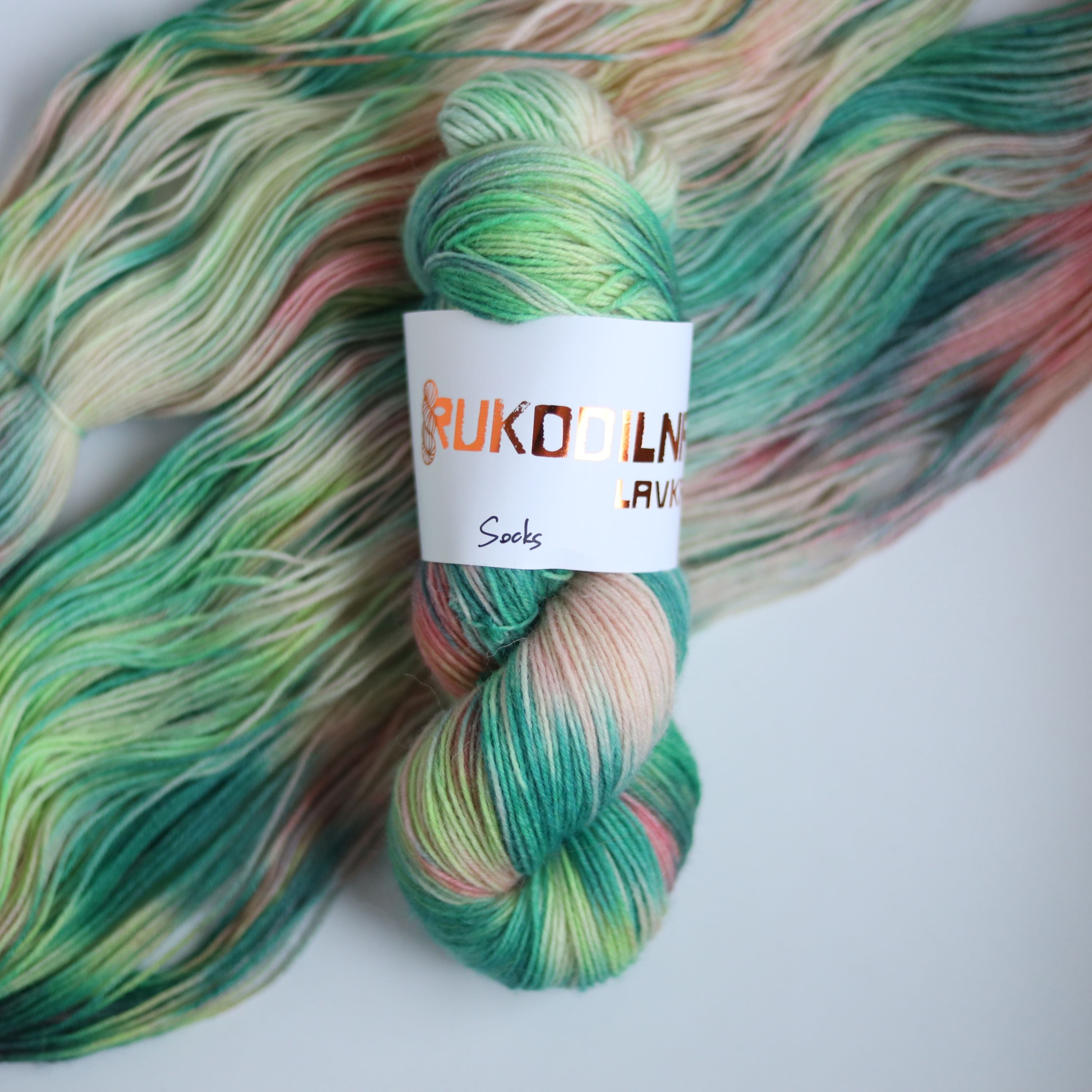 Hand dyed superwash merino sock yarn in neon green variegated shades with soft pink and beige tones on a white background