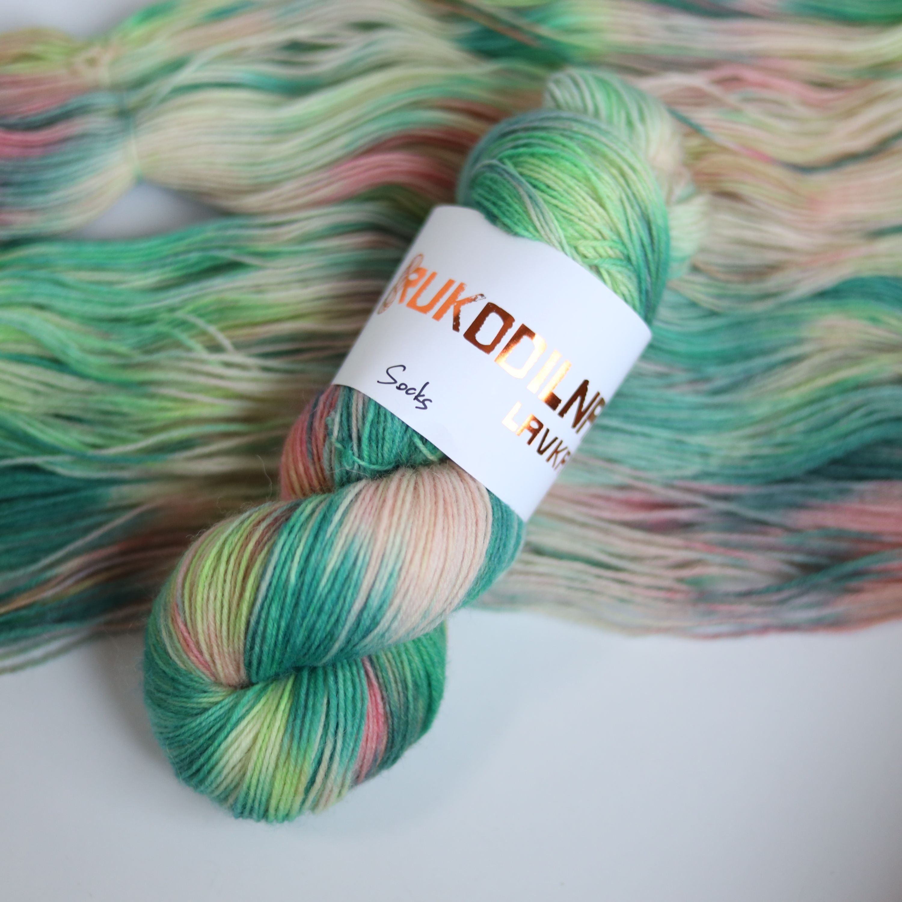 Hand dyed superwash merino sock yarn in neon green variegated shades with soft pink and beige tones on a white background