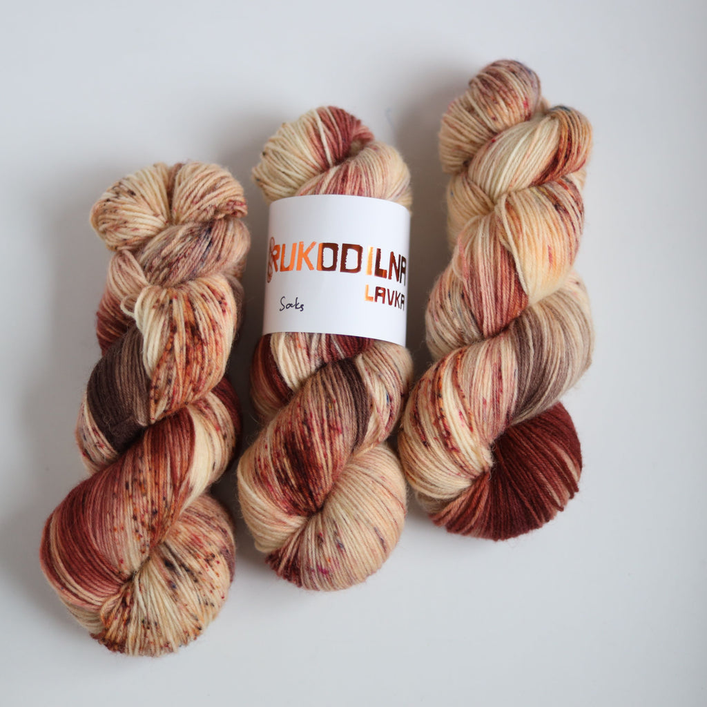 Hand dyed sock yarn skeins in warm brown and beige variegated tones on a white background