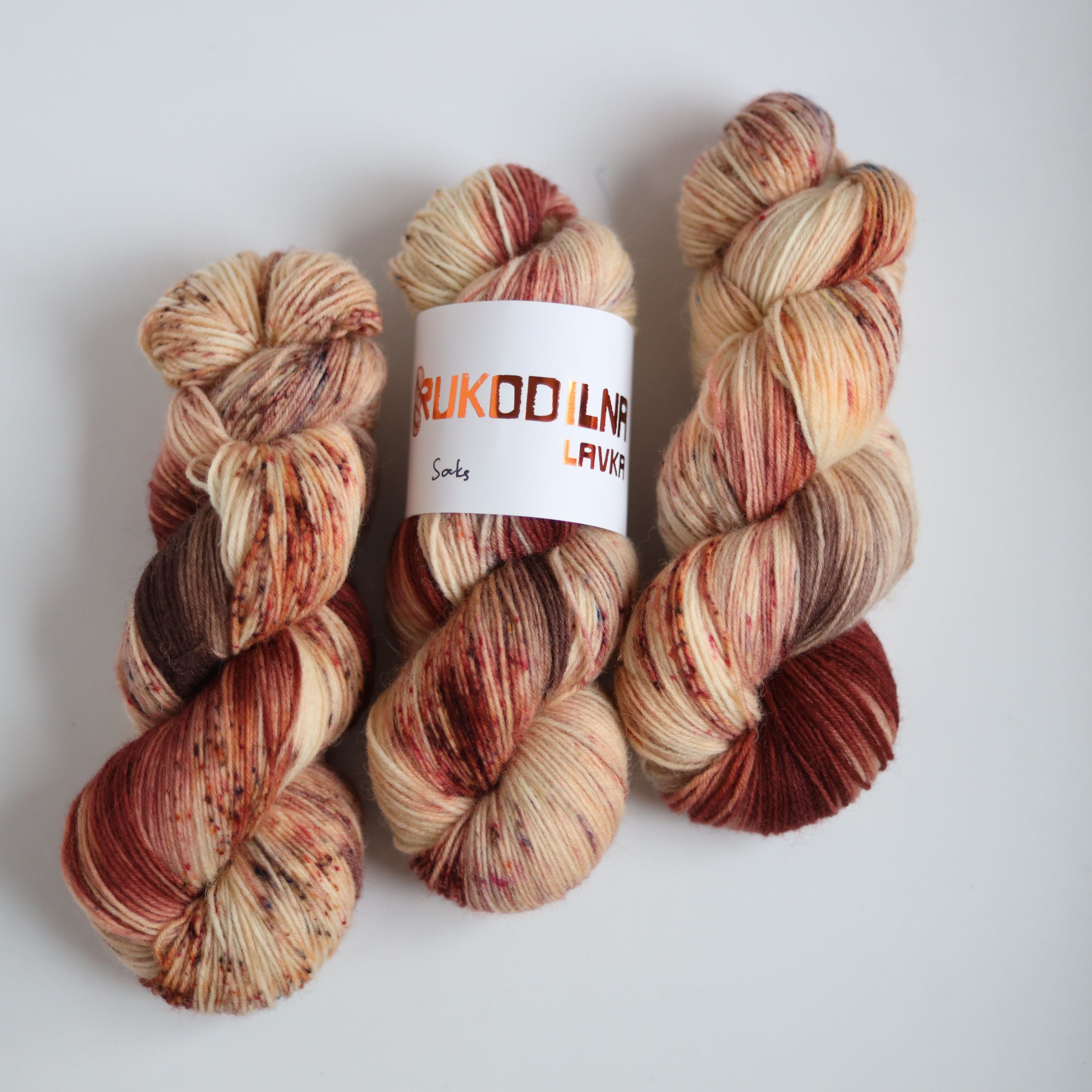 Hand dyed sock yarn skeins in warm brown and beige variegated tones on a white background