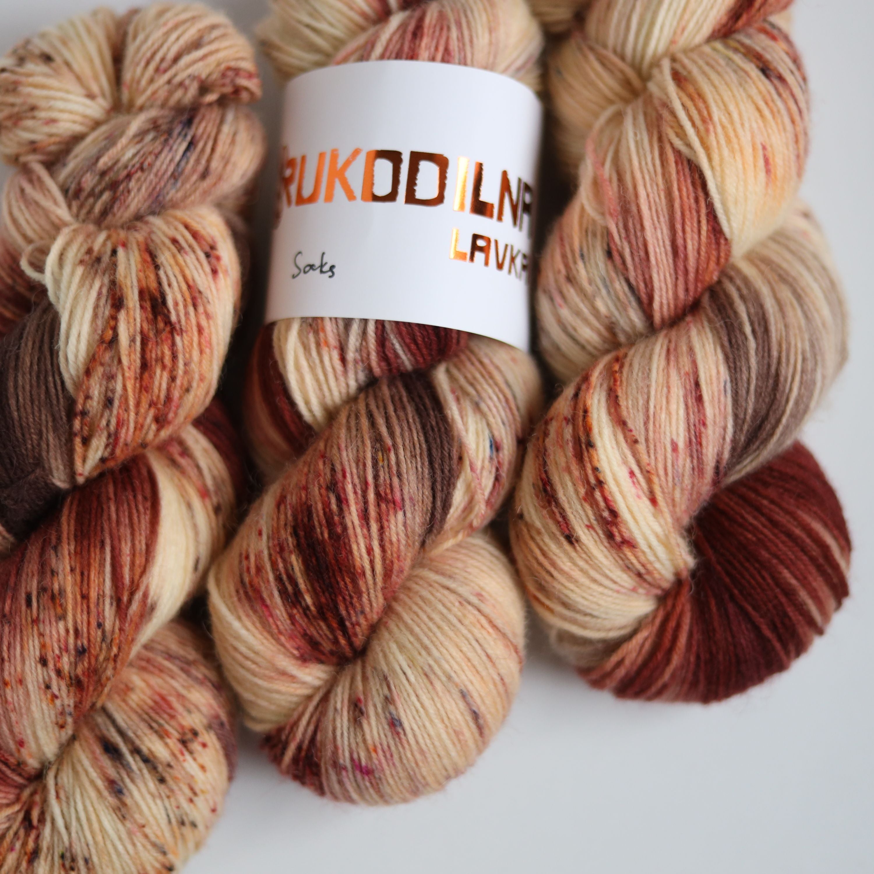 Hand dyed sock yarn skeins in warm brown and beige variegated tones on a white background