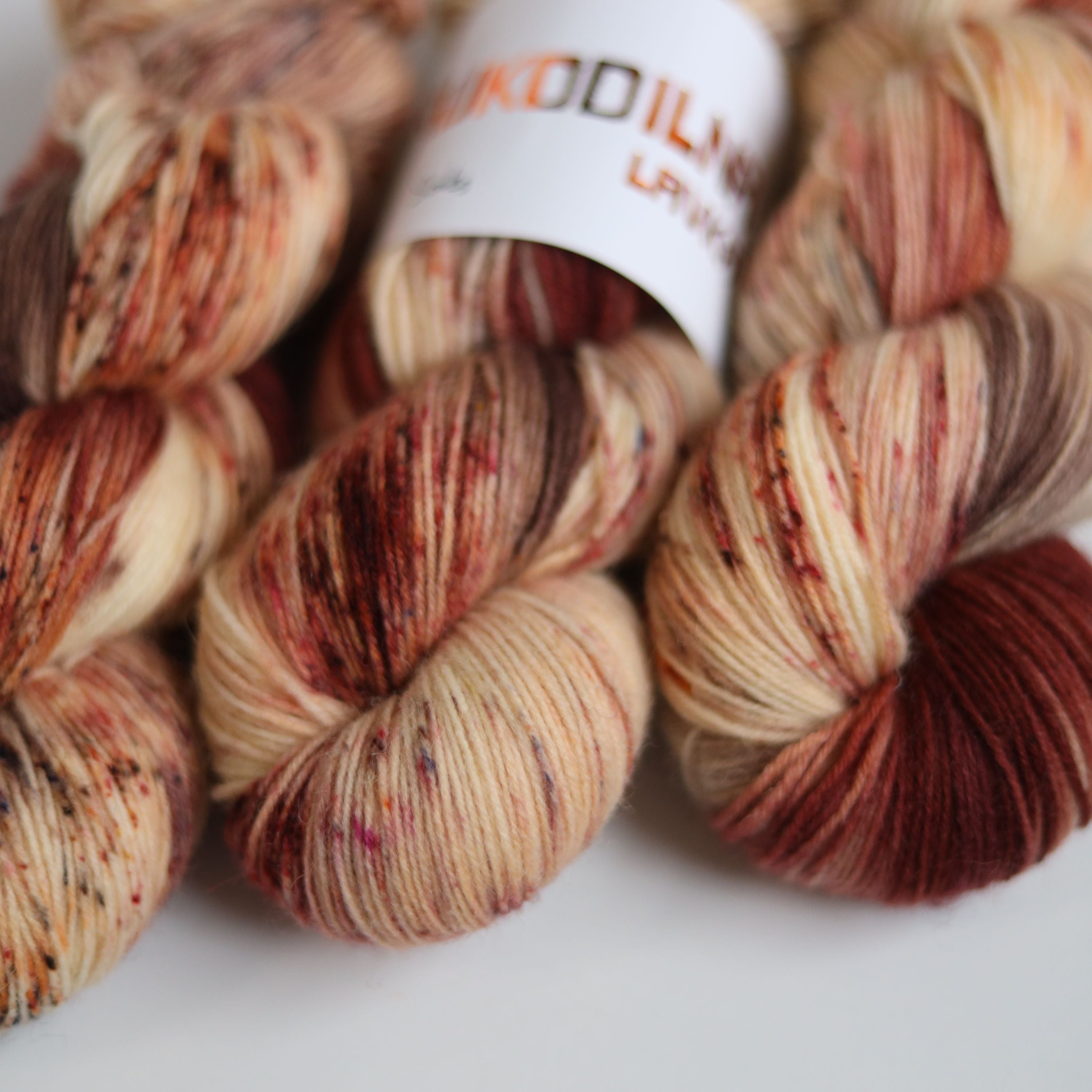 Hand dyed sock yarn skeins in warm brown and beige variegated tones on a white background