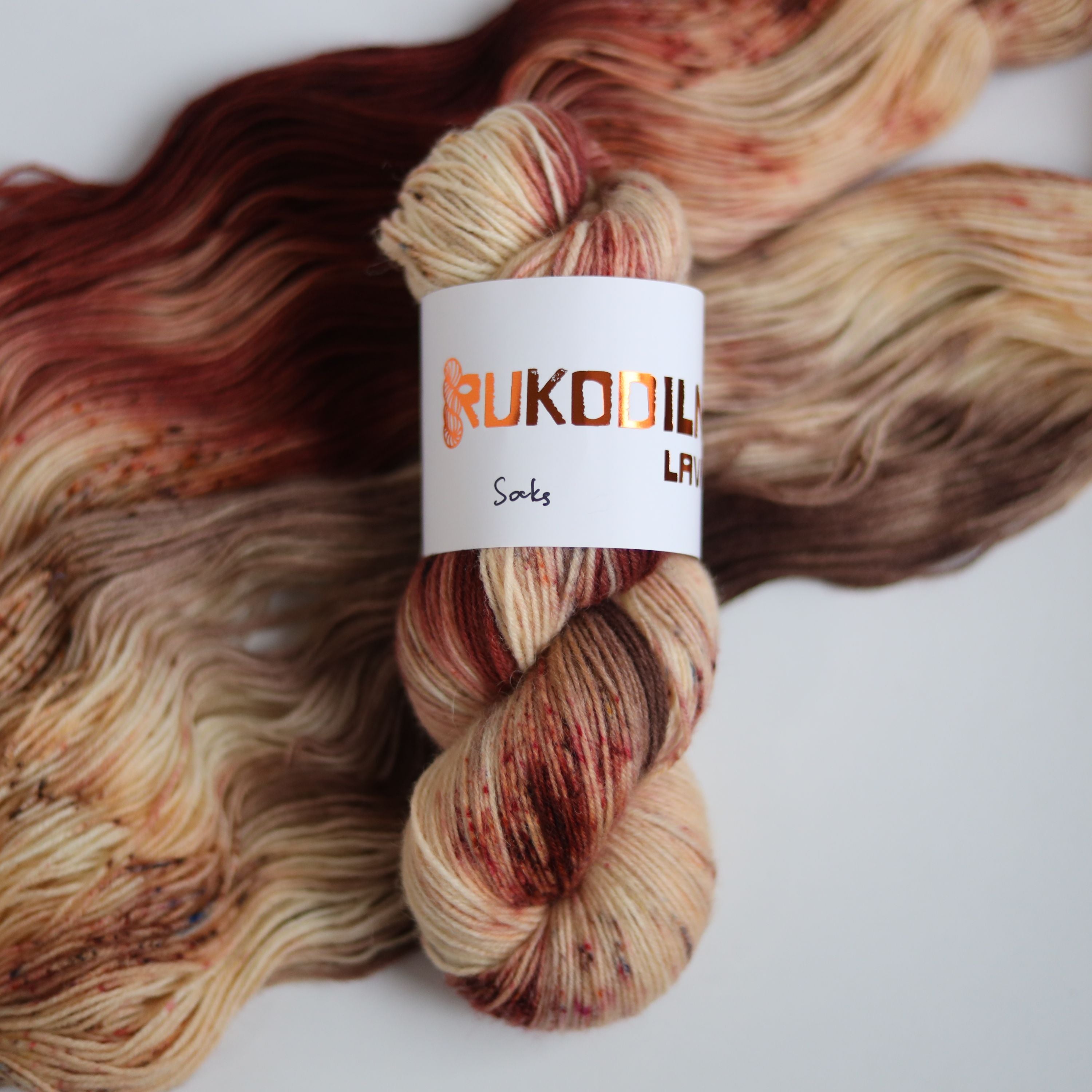 Hand dyed sock yarn skeins in warm brown and beige variegated tones on a white background
