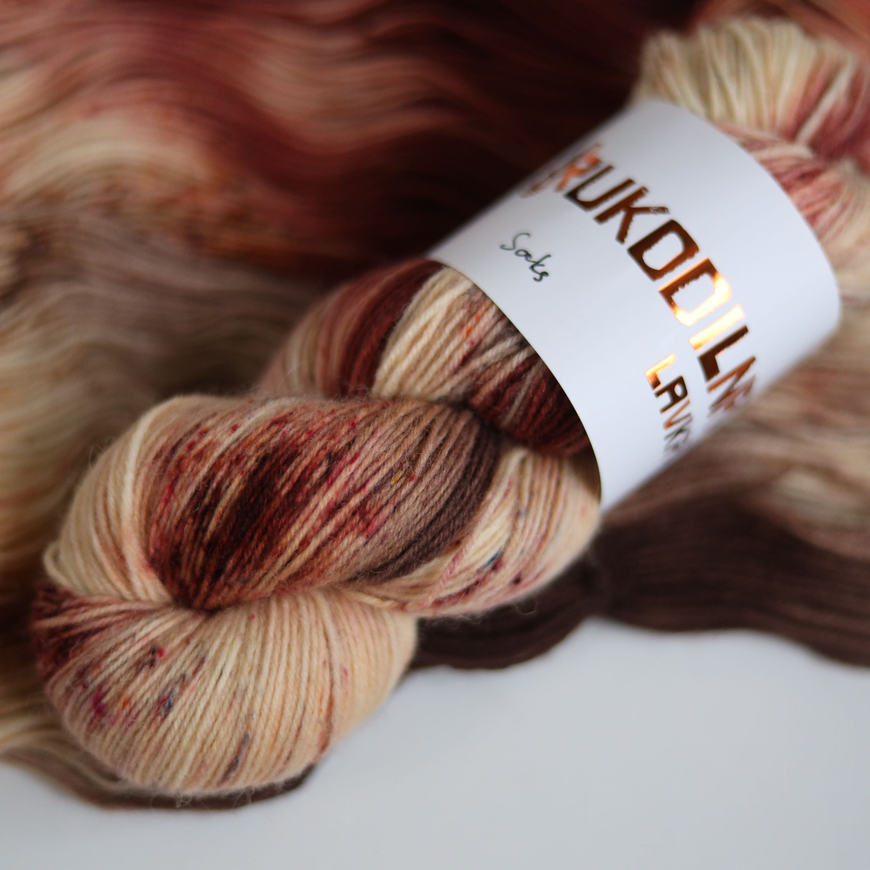 Hand dyed sock yarn skeins in warm brown and beige variegated tones on a white background