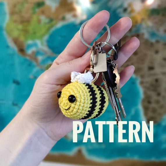 Hand holding a handmade crochet bee keychain amigurumi in front of a world map background.